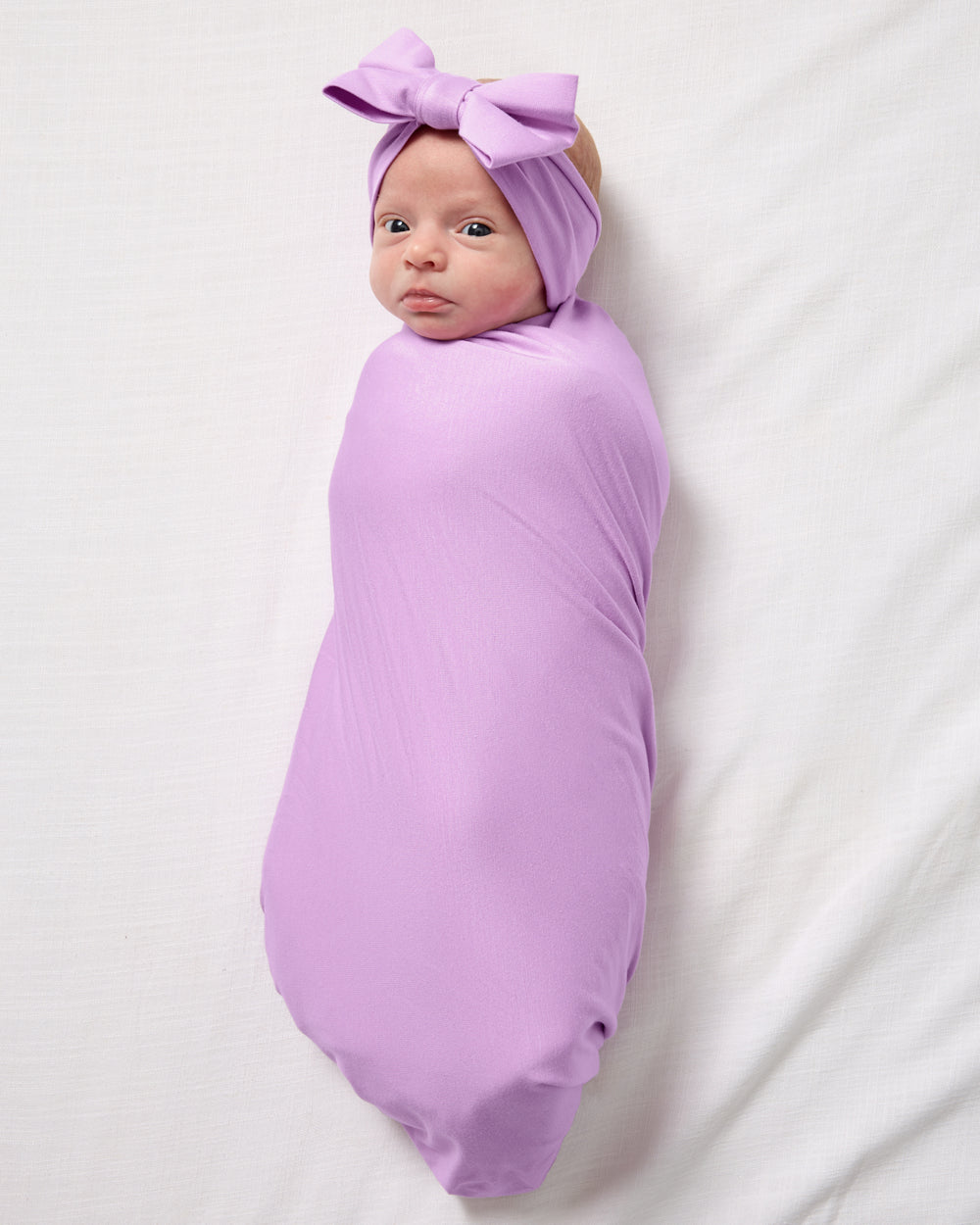 Aerial view of baby wearing the Soft Wisteria Swaddle & Luxe Bow Headband Set