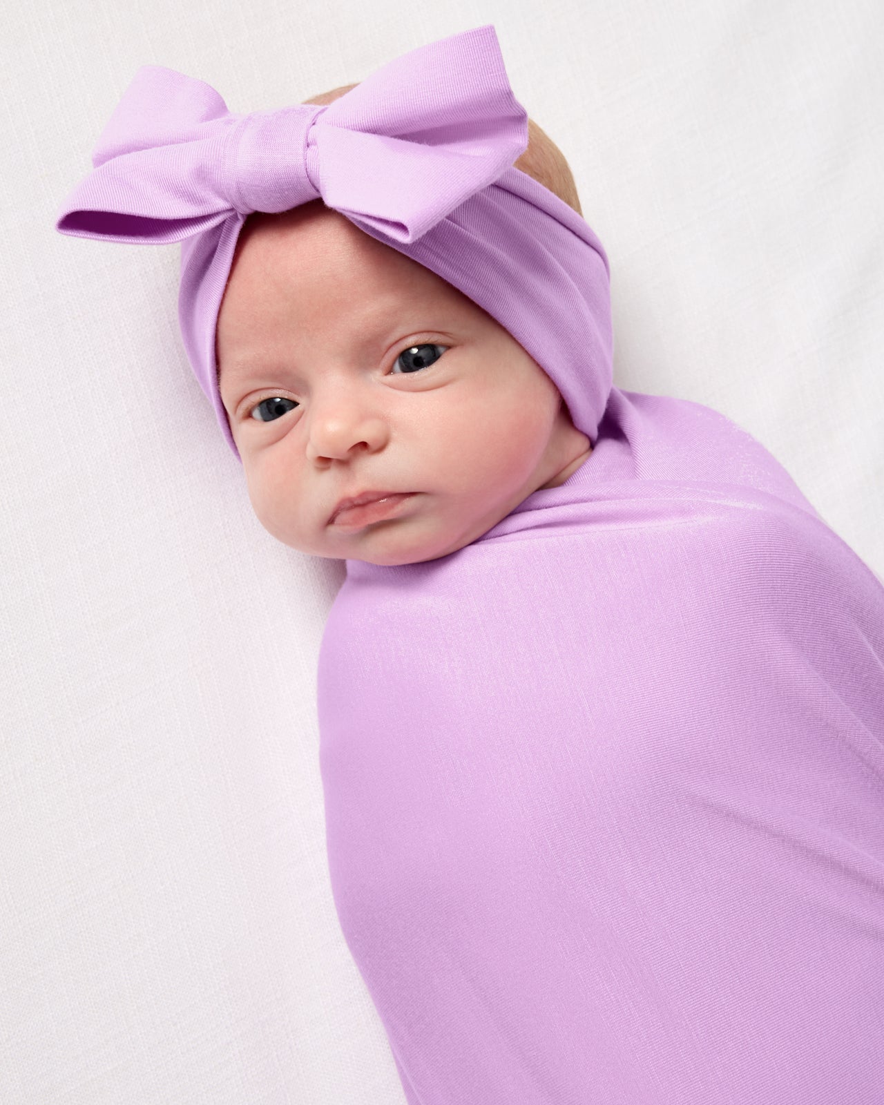 Close up of baby wearing the Soft Wisteria Swaddle & Luxe Bow Headband Set