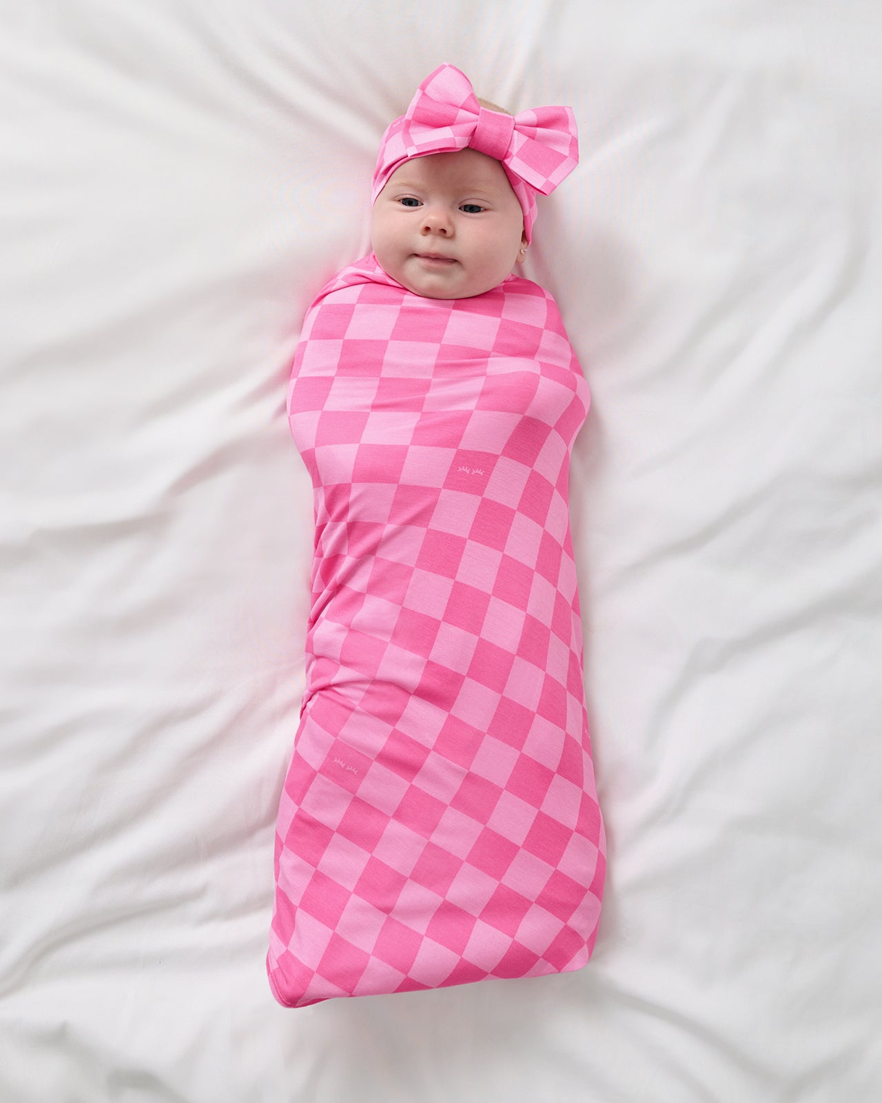 Aerial view of baby swaddled in the Sweet Raspberry Checks Swaddle & Luxe Bow Headband Set