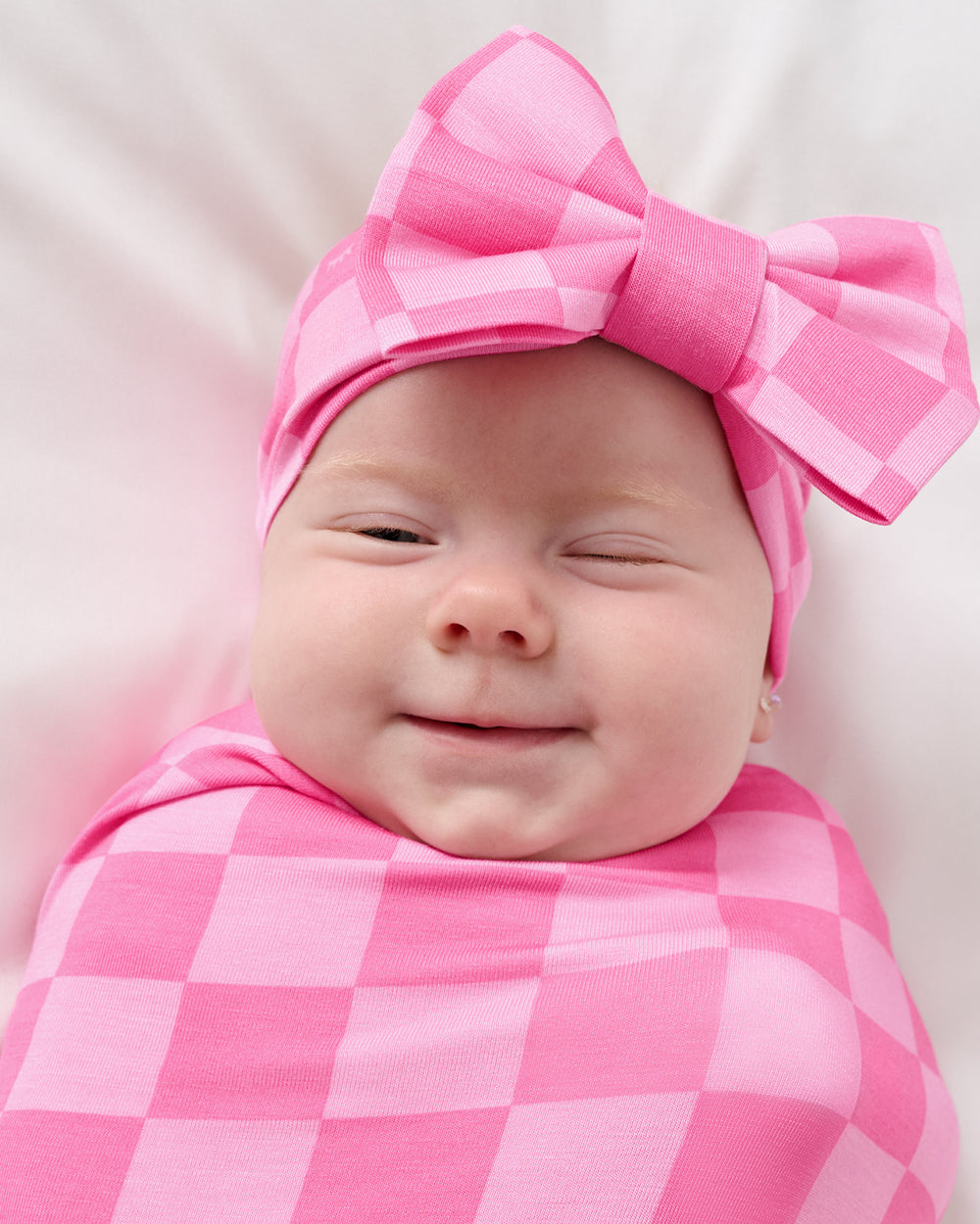 Close up of baby wearing the Sweet Raspberry Checks Swaddle & Luxe Bow Headband Set
