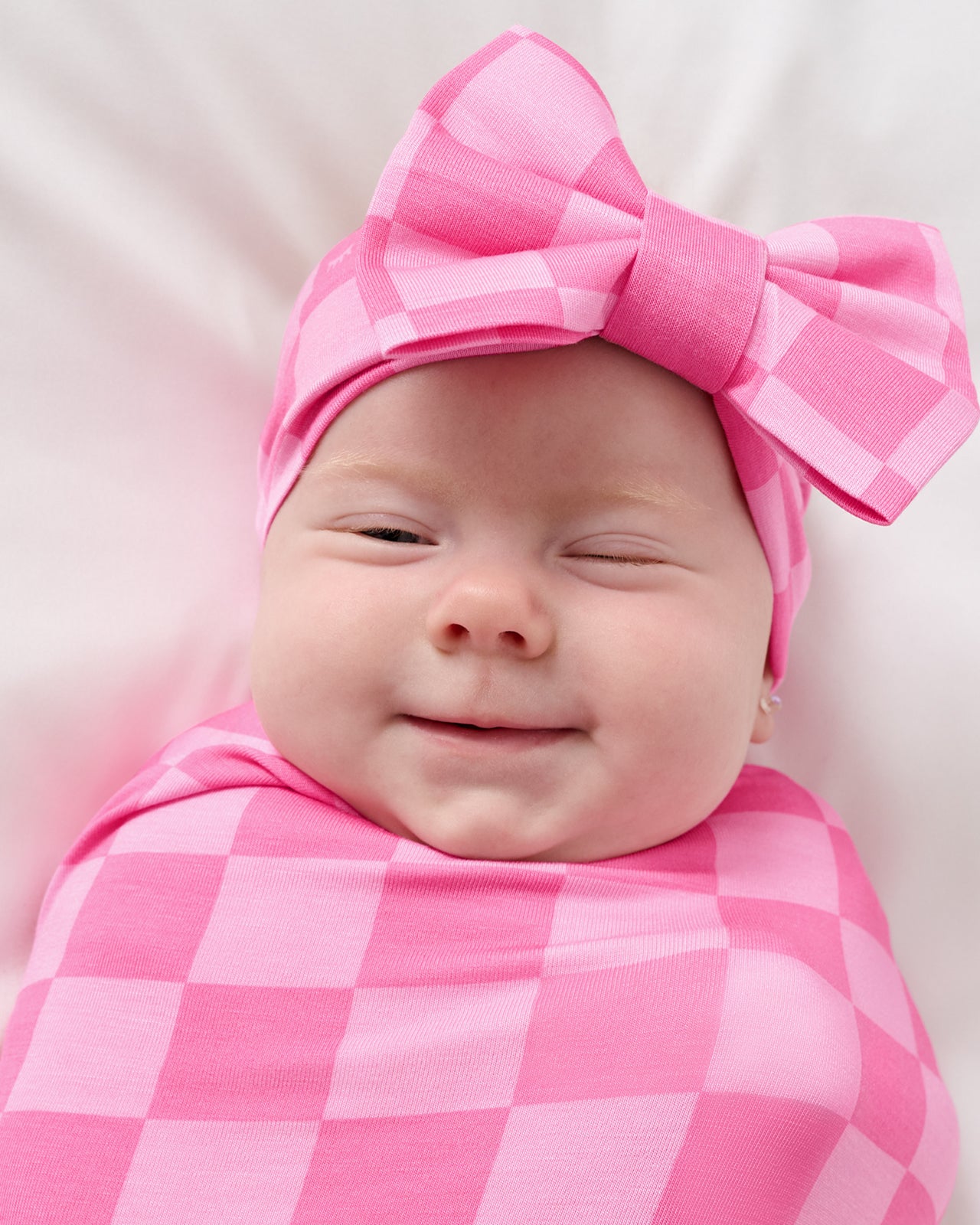 Close up of baby wearing the Sweet Raspberry Checks Swaddle & Luxe Bow Headband Set