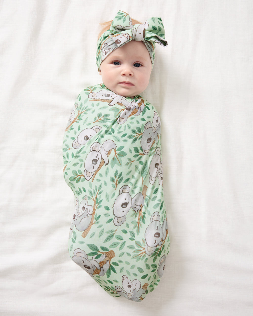 Aerial view of baby wearing the Koala Cuddles Swaddle & Luxe Bow Headband Set