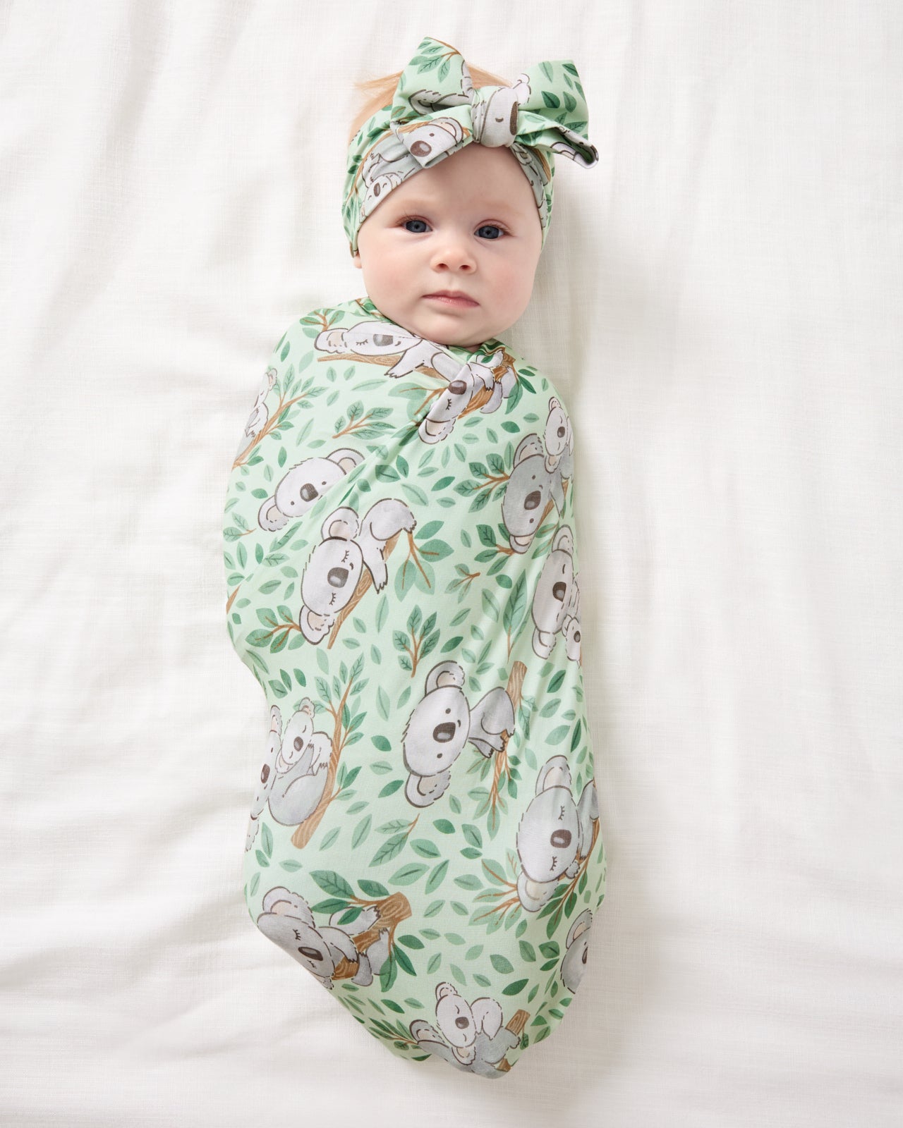 Aerial view of baby wearing the Koala Cuddles Swaddle & Luxe Bow Headband Set