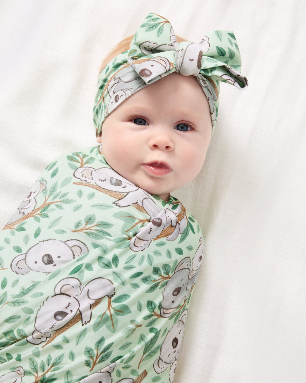 Close up of newborn wrapped in the Koala Cuddles Swaddle & Luxe Bow Headband Set