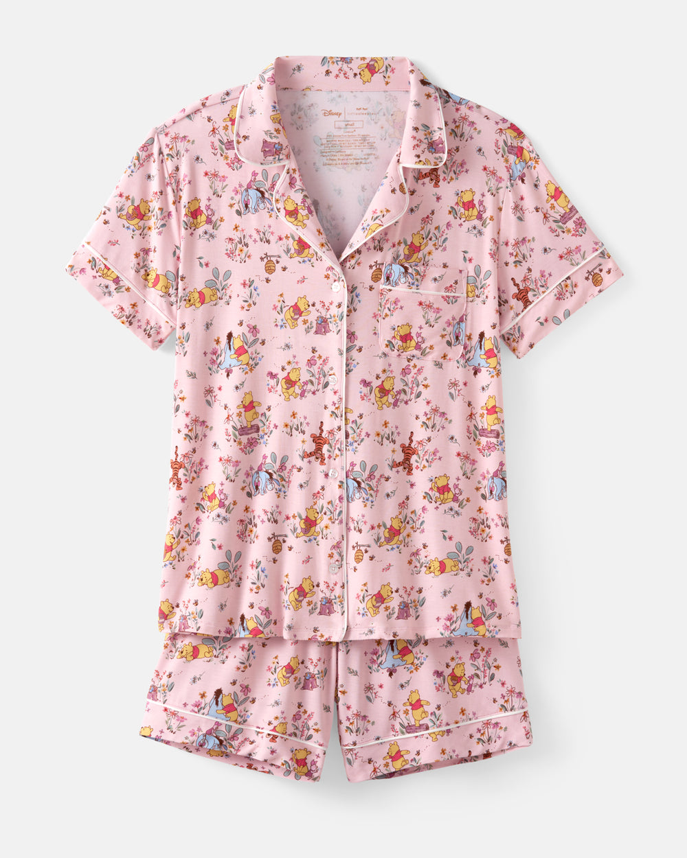 A two-piece short-sleeve pajama set in light pink with a colorful whimsical character print, featuring a button-up shirt and matching shorts with white piping details.