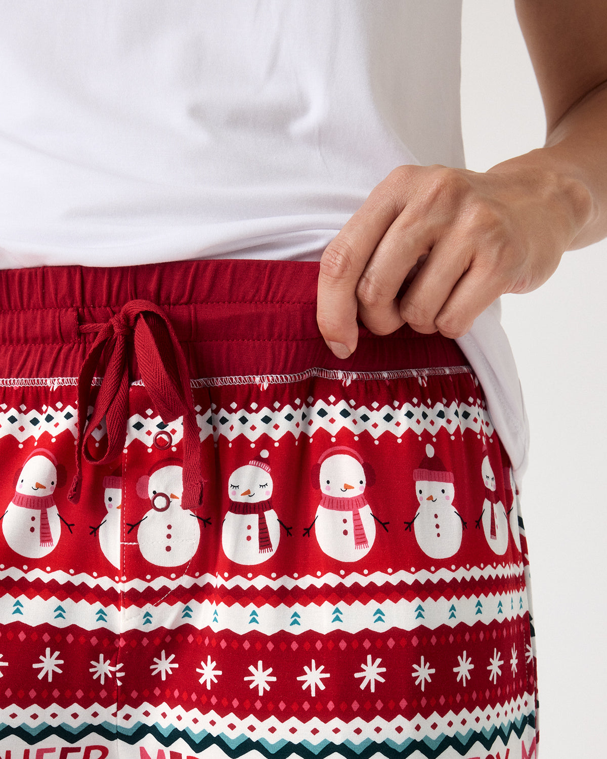 A close-up of a person wearing red holiday drawstring shorts with a white snowman pattern and a white t-shirt, against a plain white background.