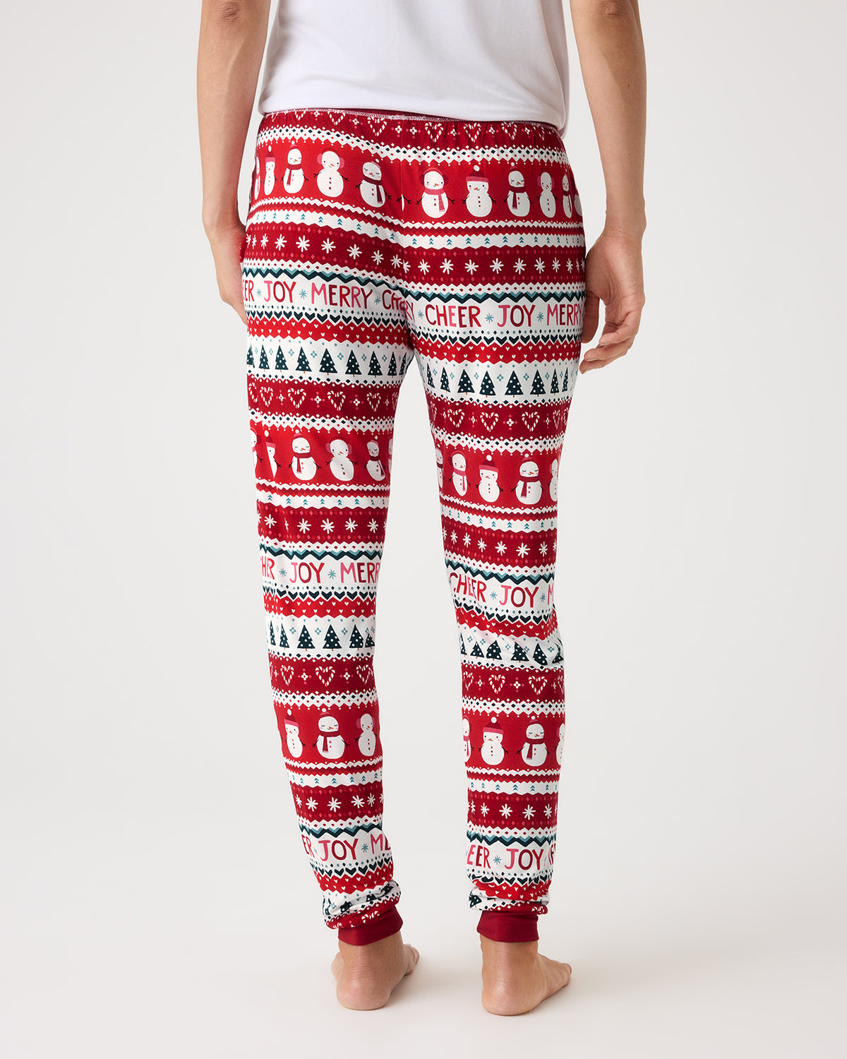 A person shown from the back wearing red holiday leggings with a white and black Christmas pattern featuring snowmen, trees, hearts, and text like 'MERRY' and 'CHEER'.