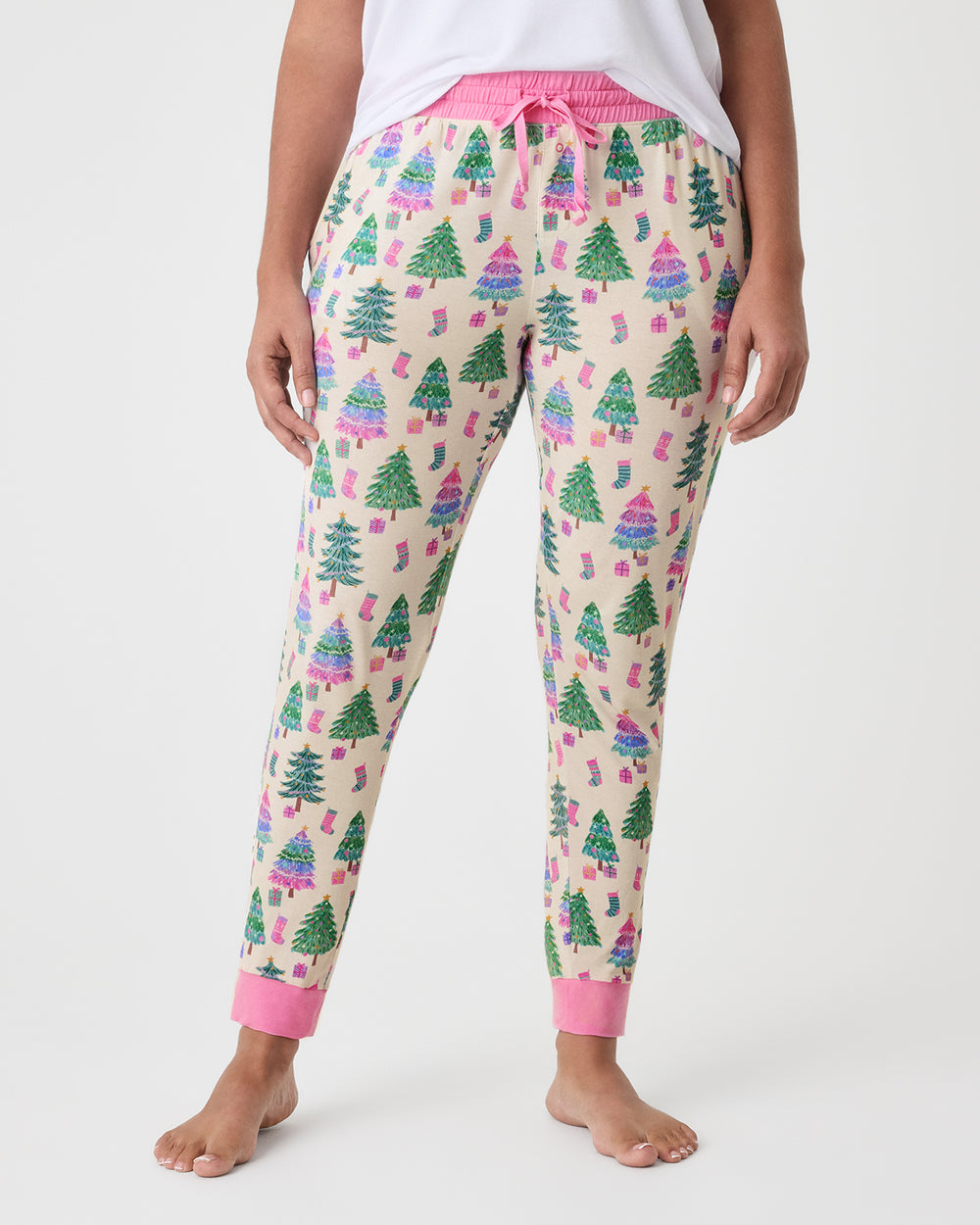 A person wearing patterned pajama pants with a Christmas tree print, shown from the waist down against a light gray studio background.