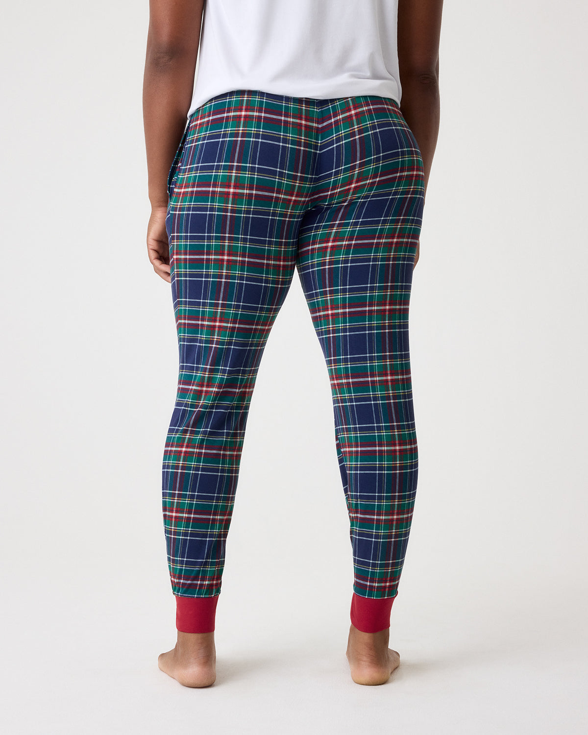 Rear view of a person wearing plaid leggings with a navy base and red, green, and white tartan lines, paired with a white top, against a light gray studio background.