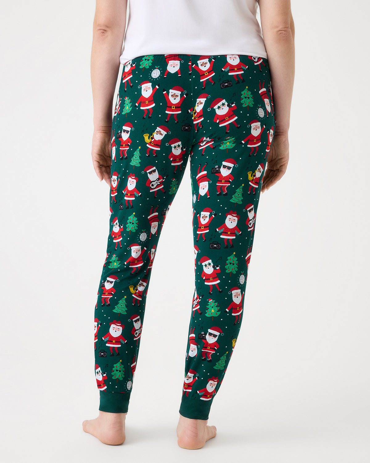 A person shown from the back wearing dark green Christmas pajama pants with an all-over Santa Claus print, against a plain light gray studio background.