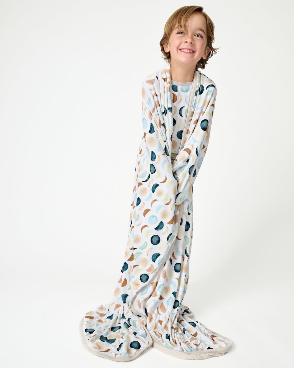 Standing boy wrapped in the Luna Neutral Large Cloud Blanket®