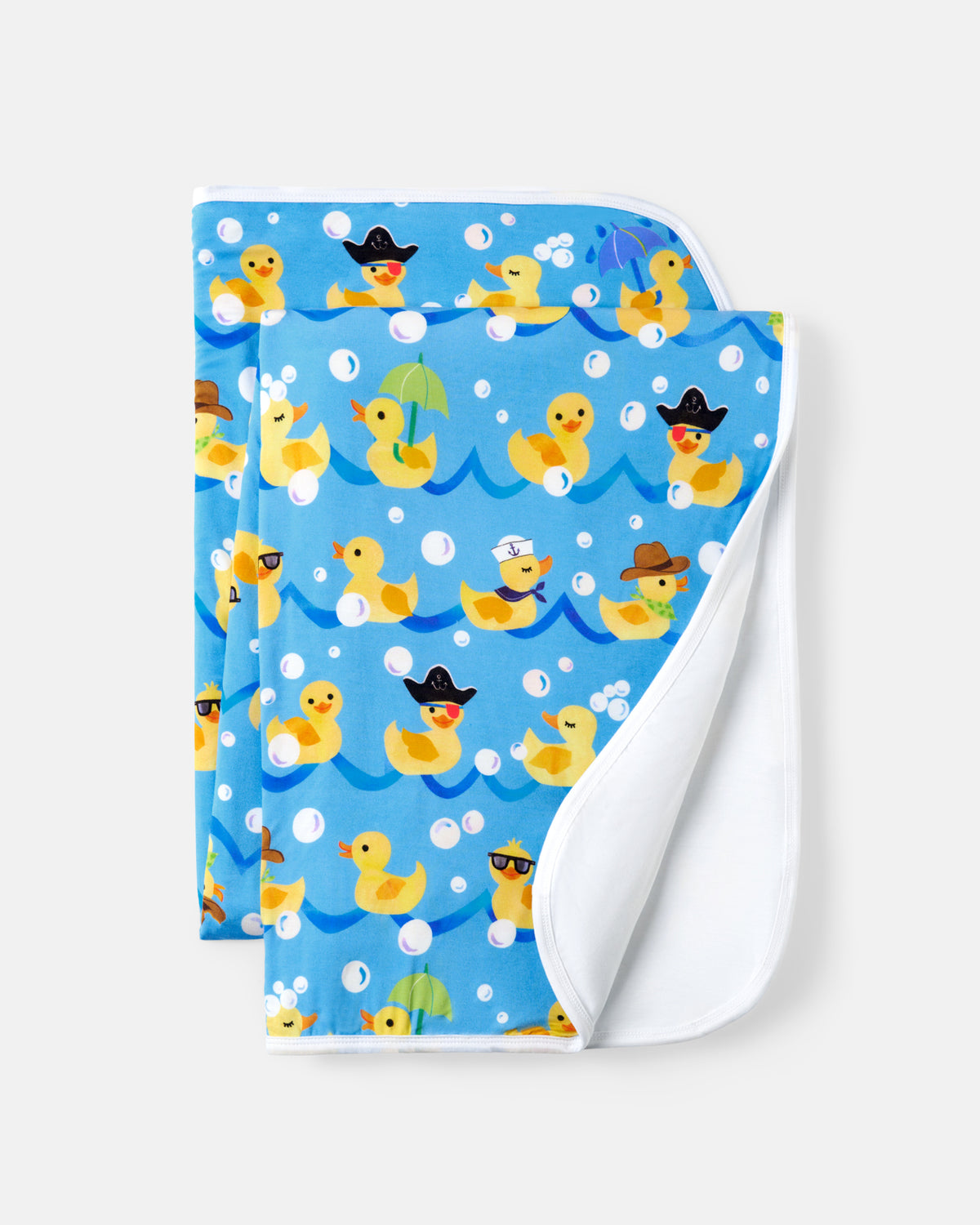 A folded kids blanket with a blue background featuring a playful pattern of yellow rubber ducks in various poses, with a soft white reverse side, shown on a light gray background.