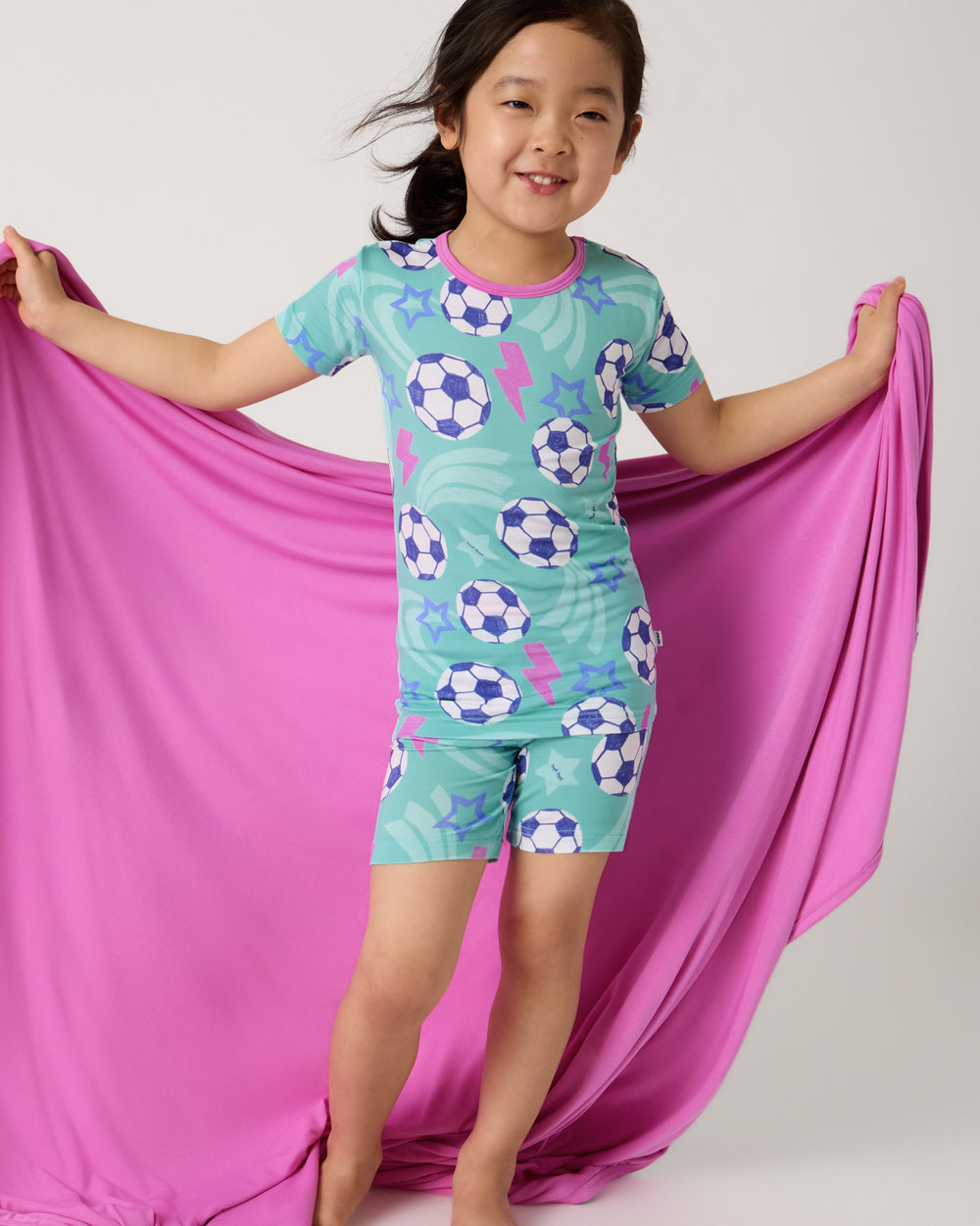 Girl wearing the Aqua Soccer Stars Two-Piece Short Sleeve & Shorts Pajama Set holding the Aqua Soccer Stars cloud blanket