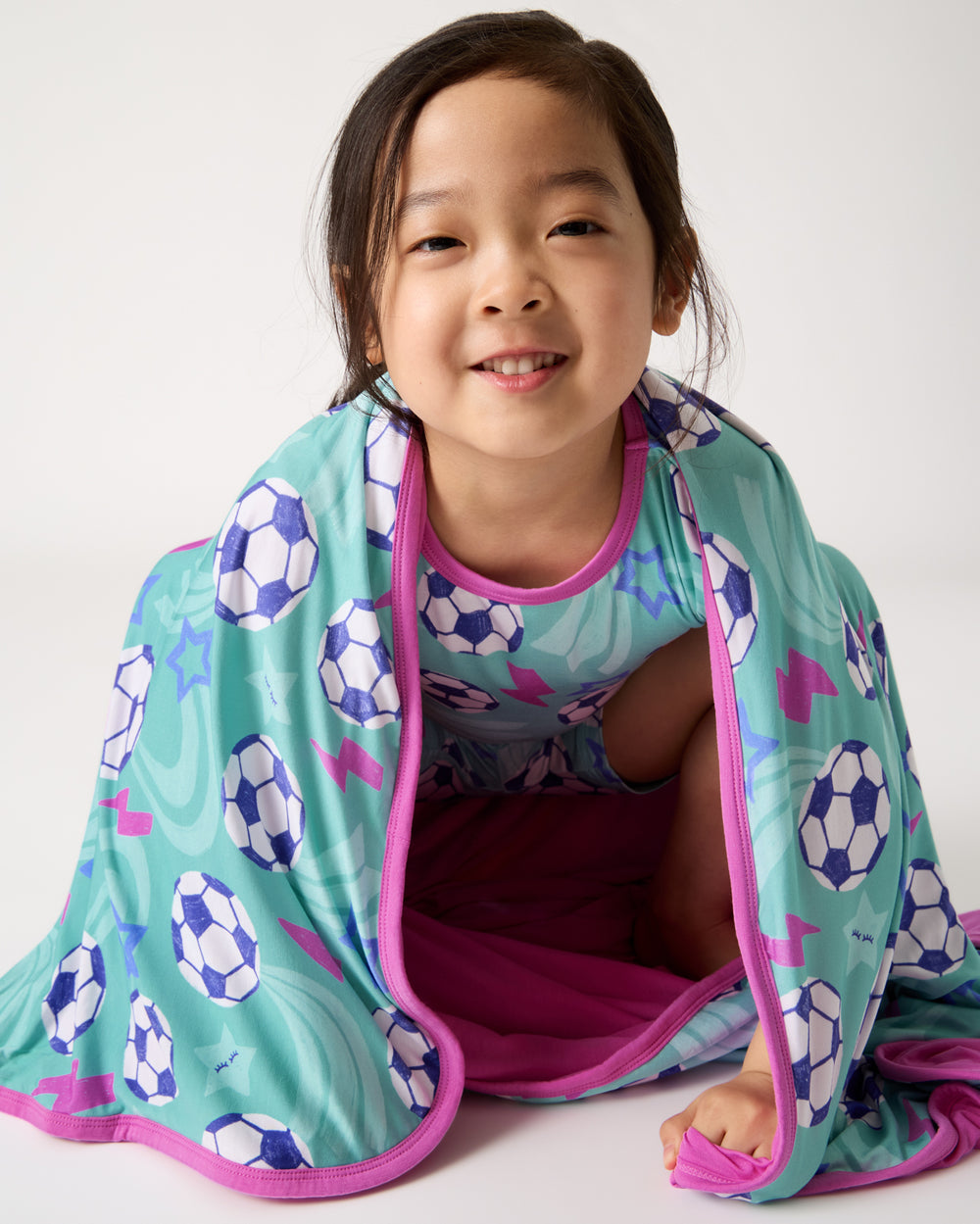Sitting girl wrapped in the Aqua Soccer Stars Large Cloud Blanket®
