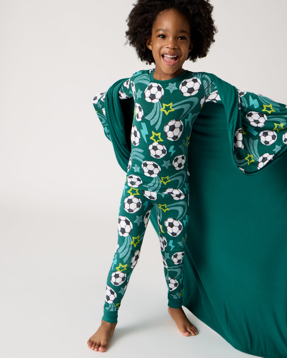 Standing boy wearing the Soccer Stars Two-Piece Pajama Set wrapped in the Soccer Stars Blanket