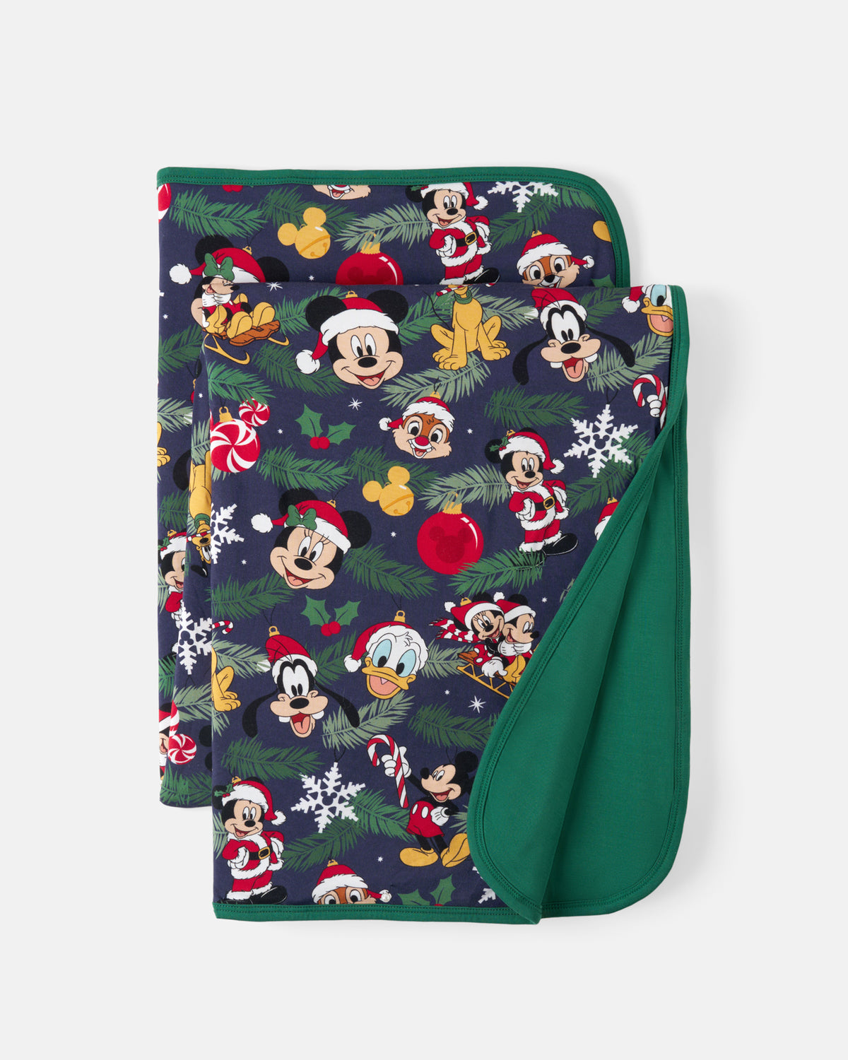 A folded blanket featuring a festive Christmas print with Disney characters Mickey Mouse, Minnie Mouse, Goofy, and Donald Duck wearing Santa hats, set against a dark navy background with green pine branches, white snowflakes, and red ornaments. The reverse side is solid dark green.