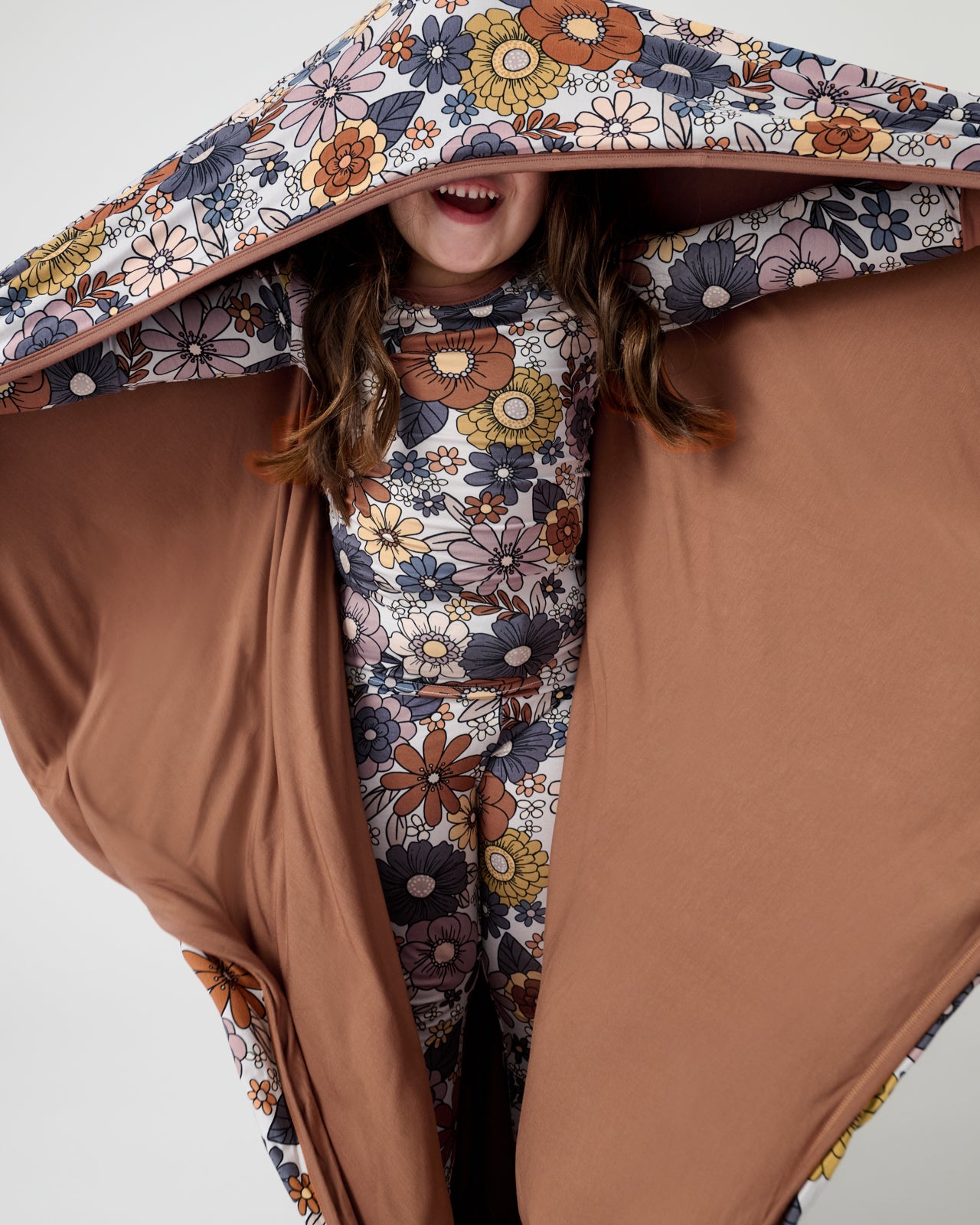 Girl holding out the Wildwood Floral Large Cloud Blanket® showing the solid brown side