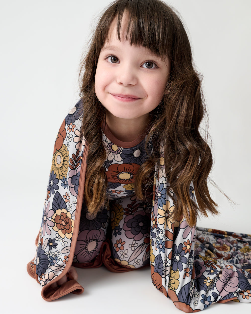 Sitting girl wrapped in the Wildwood Floral Large Cloud Blanket®