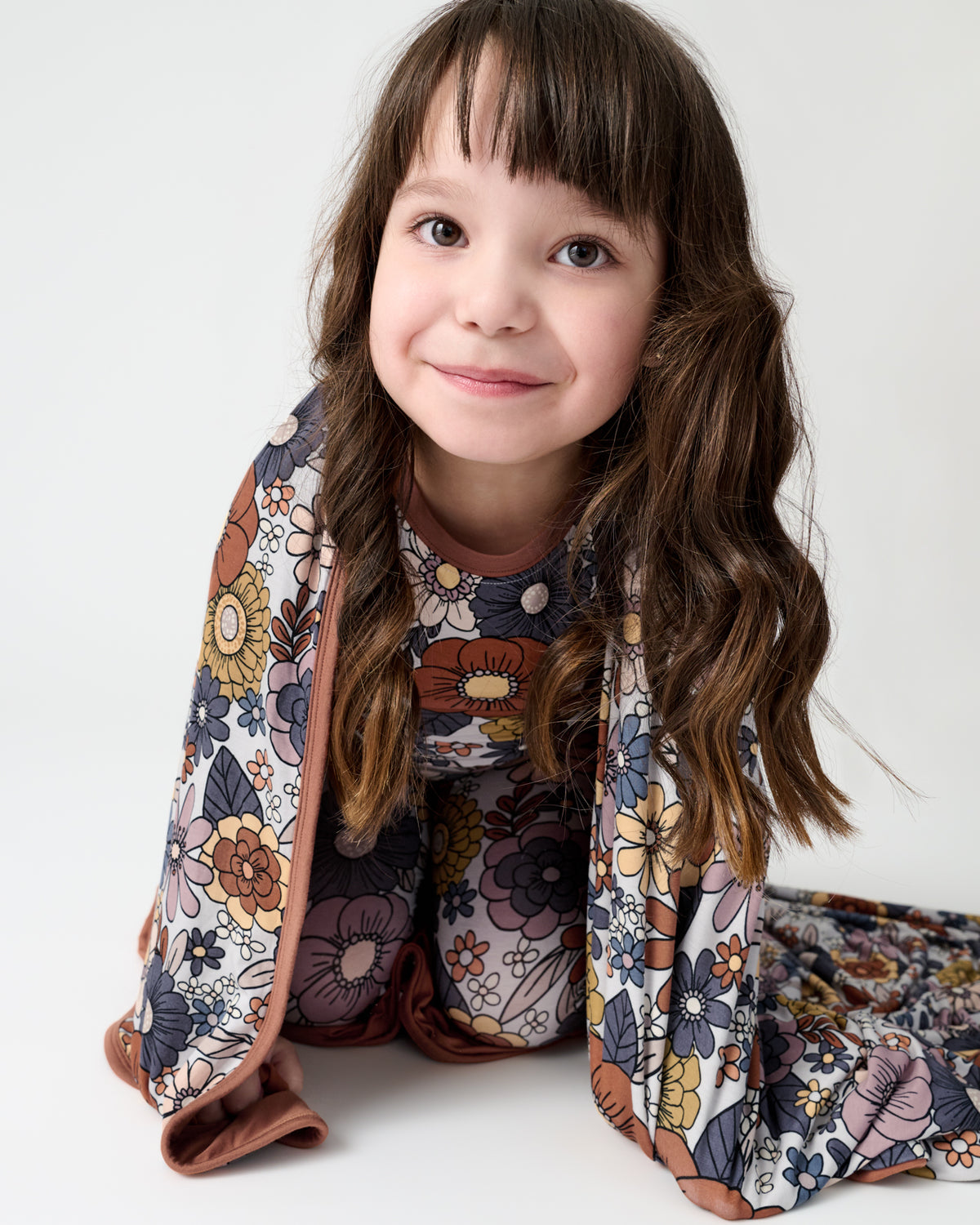 Sitting girl wrapped in the Wildwood Floral Large Cloud Blanket®