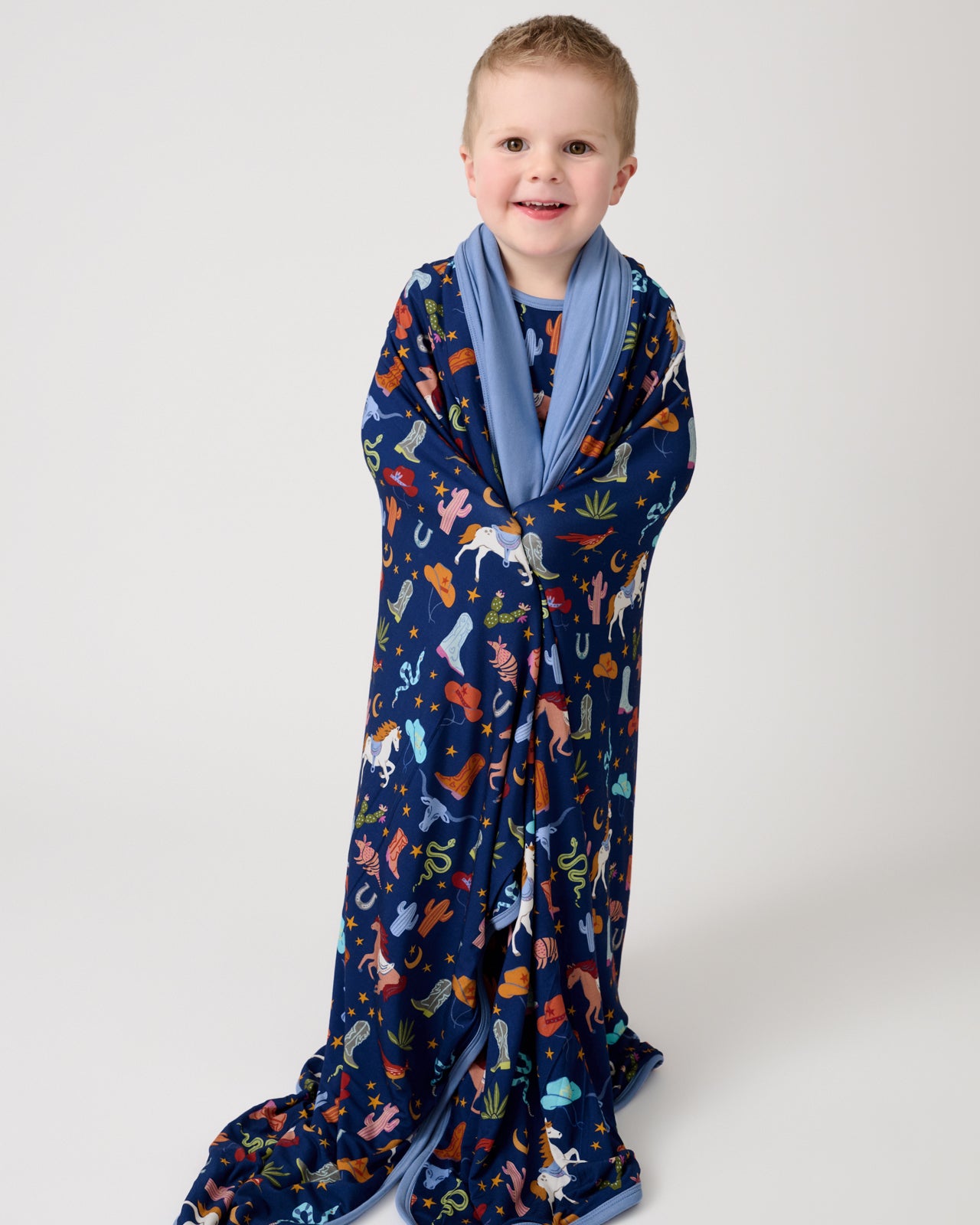 Standing boy wrapped in the Blue Rancher Roundup Large Cloud Blanket®