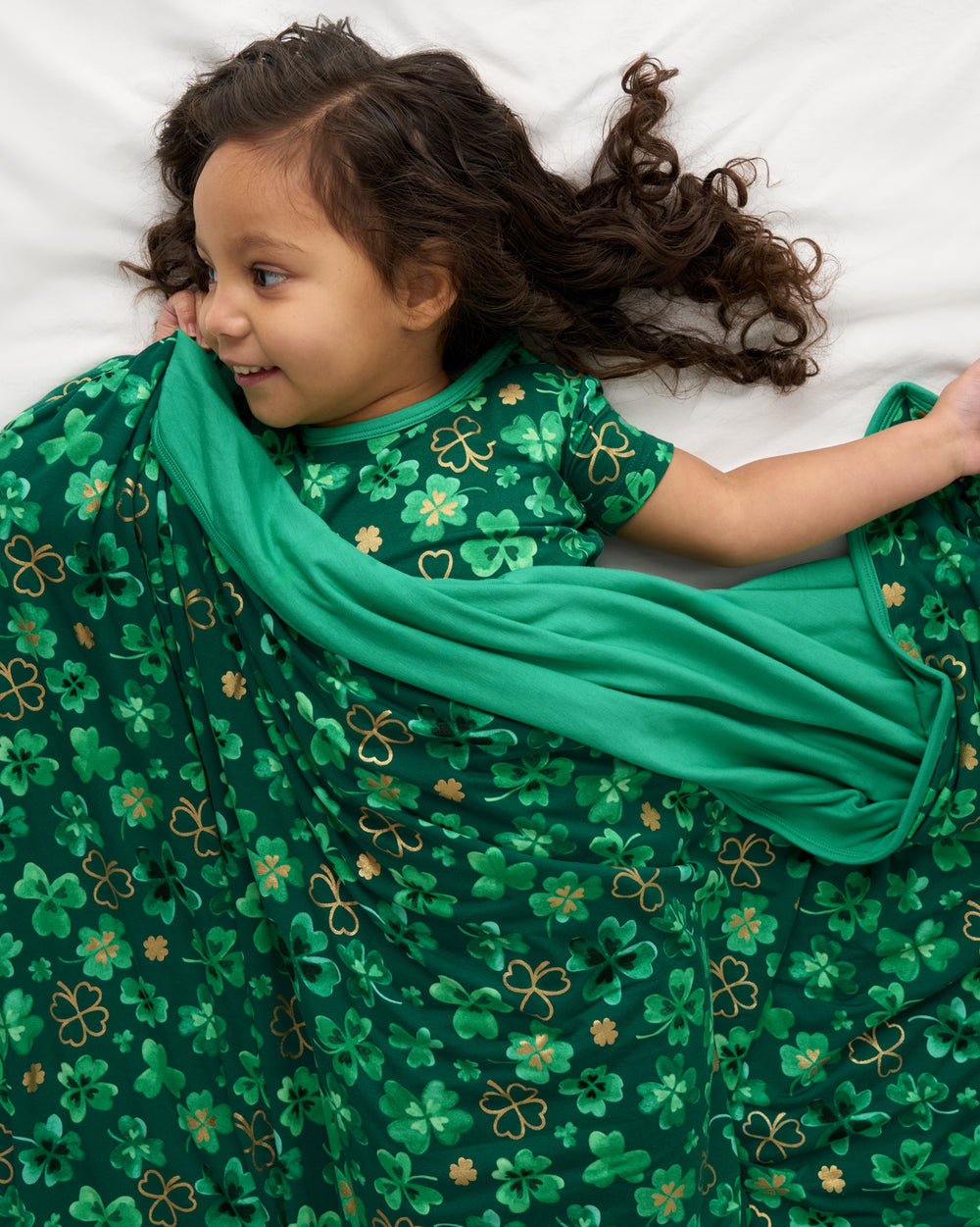 Child laying on a bed covered with the Clover Cuties Large Cloud Blanket®