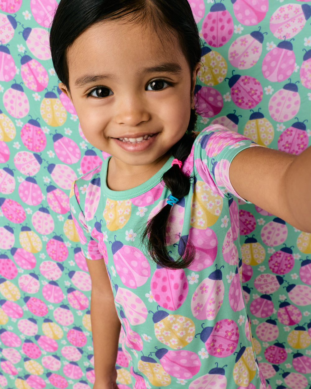 Close up of girl wearing the Ladybug Meadow Two-Piece Short Sleeve & Shorts Pajama Set with a ladybug print background