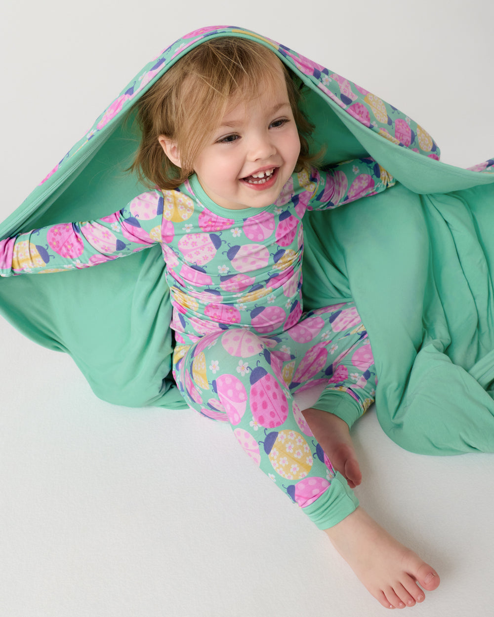 Child sitting with the Ladybug Meadow Large Cloud Blanket® draped over her