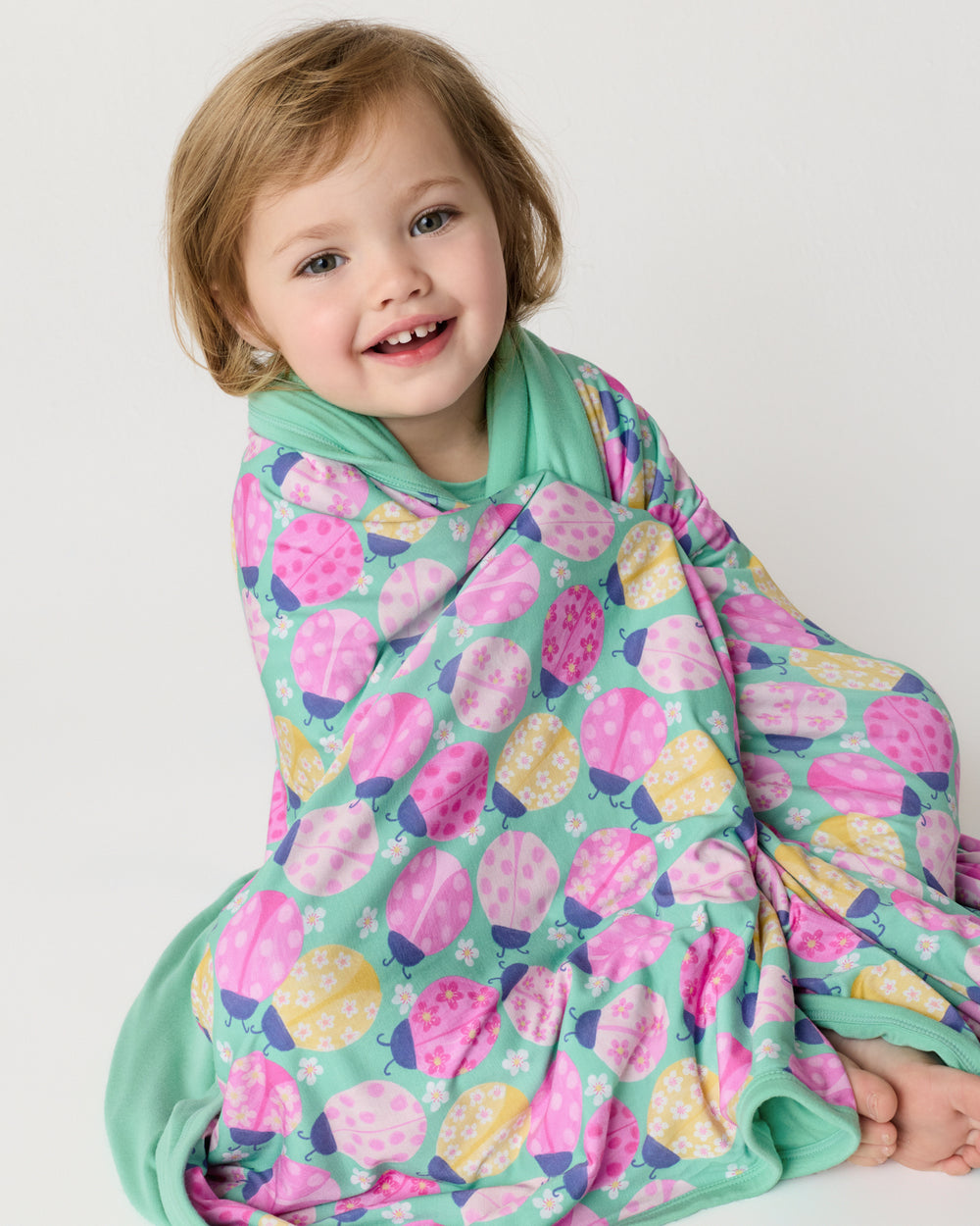 Sitting child wrapped in the Ladybug Meadow Large Cloud Blanket®