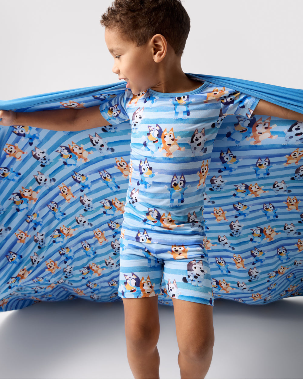 Boy holding up the Bluey Dance All Day Large Cloud Blanket® wearing matching pajamas