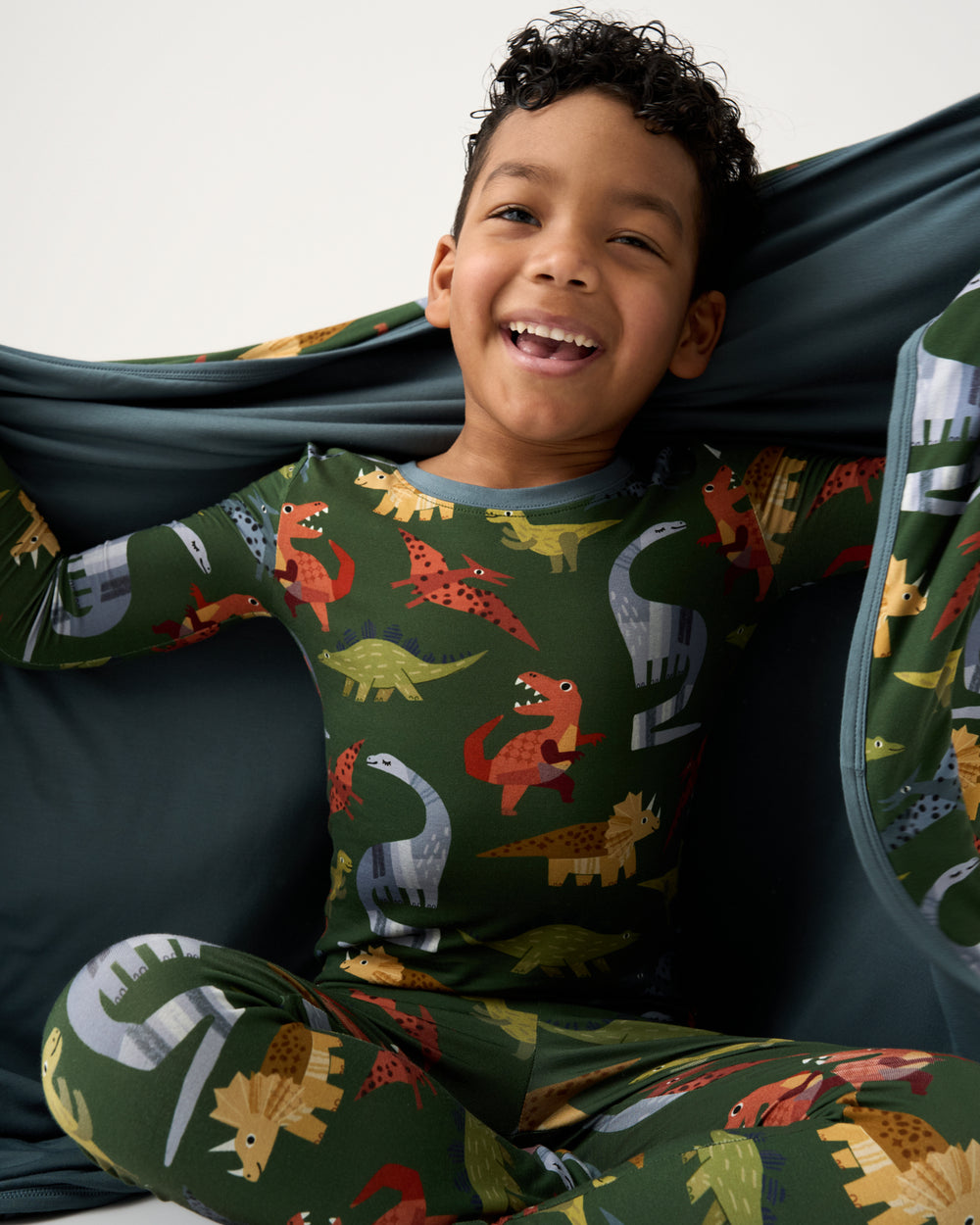 Sitting boy holding the Green Roar & Explore Large Cloud Blanket® wearing matching PJs