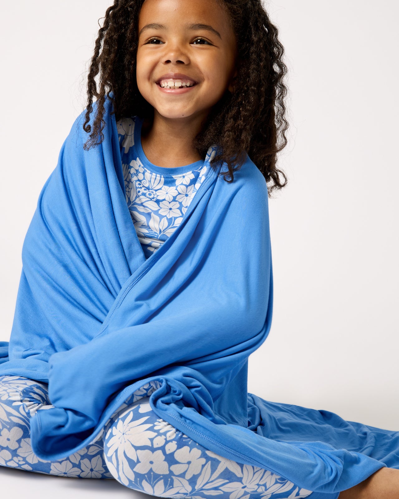 Sitting girl wrapped in the Azure Garden Large Cloud Blanket®