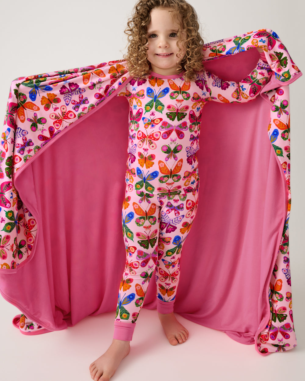 Girl holding out the Flutter Garden Large Cloud Blanket® showing the solid pink side