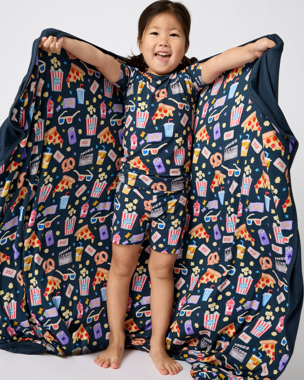 Child holding out the Movie Marathon Large Cloud Blanket® wearing matching PJs