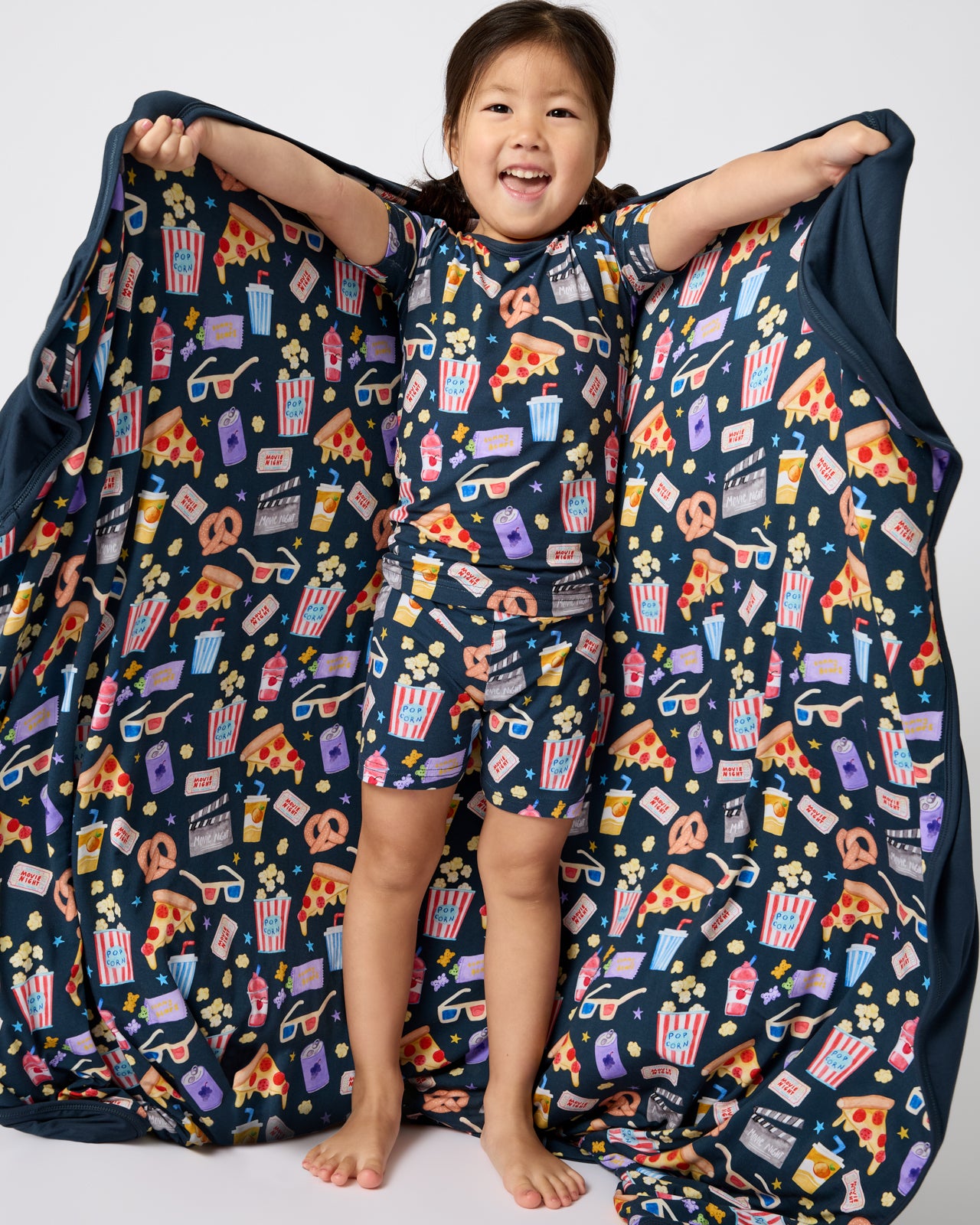 Child holding out the Movie Marathon Large Cloud Blanket® wearing matching PJs