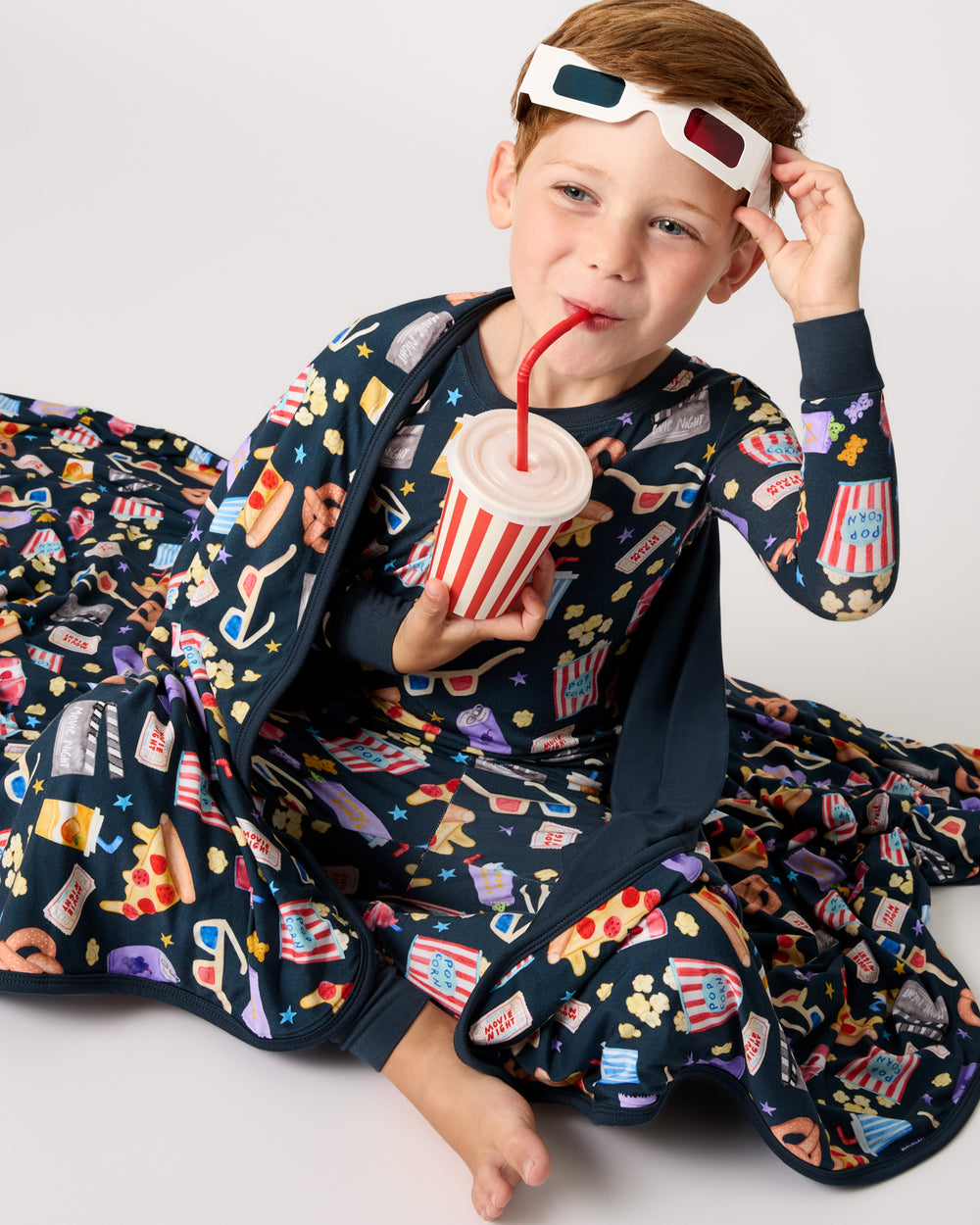 Boy sipping a drink wrapped in the Movie Marathon Large Cloud Blanket®