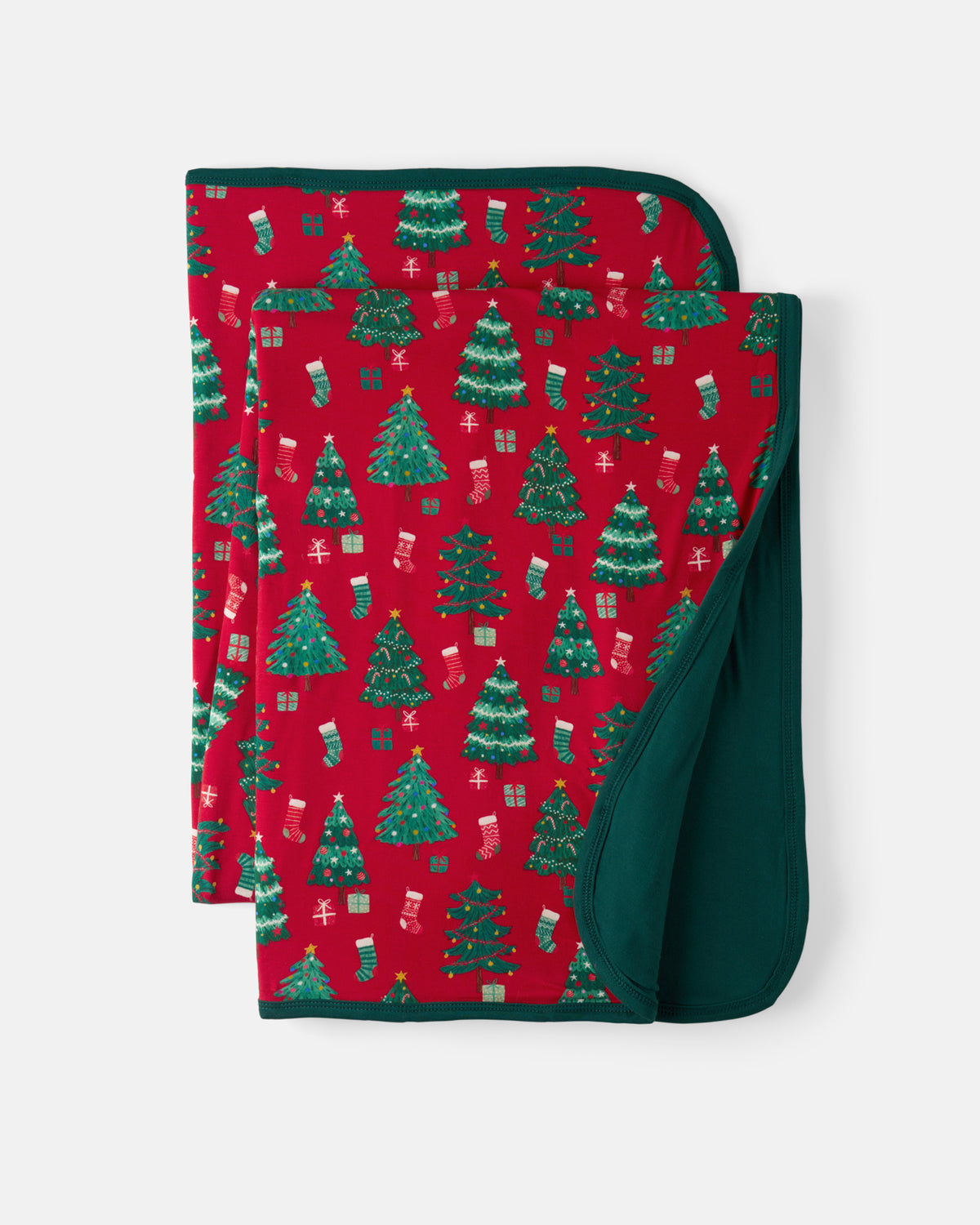 A folded baby blanket with a festive Christmas pattern featuring green trees, stockings, and gifts on a red background, with a solid dark green reverse side, shown on a light gray background.