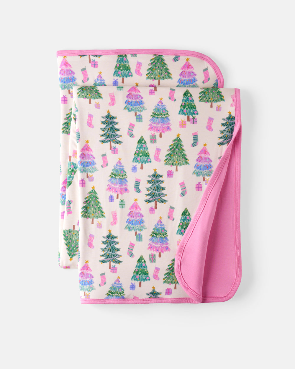 A folded baby blanket with a festive Christmas print, featuring green and pink trees, stockings, and gifts on a light pink background, with a solid pink reverse side.