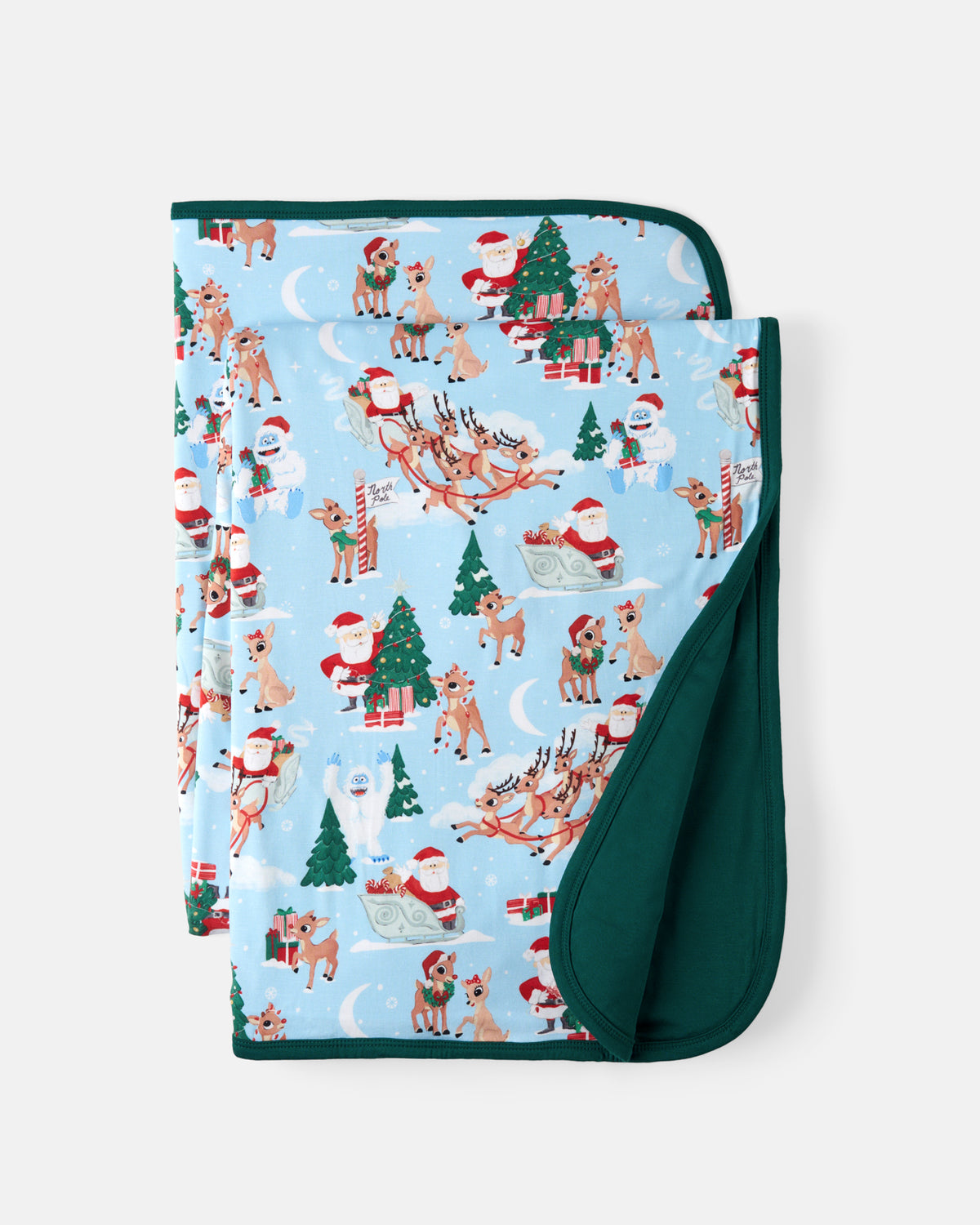 A folded baby blanket featuring a light blue Christmas print with Santa Claus, reindeer, and Christmas trees, with a solid dark green reverse side.