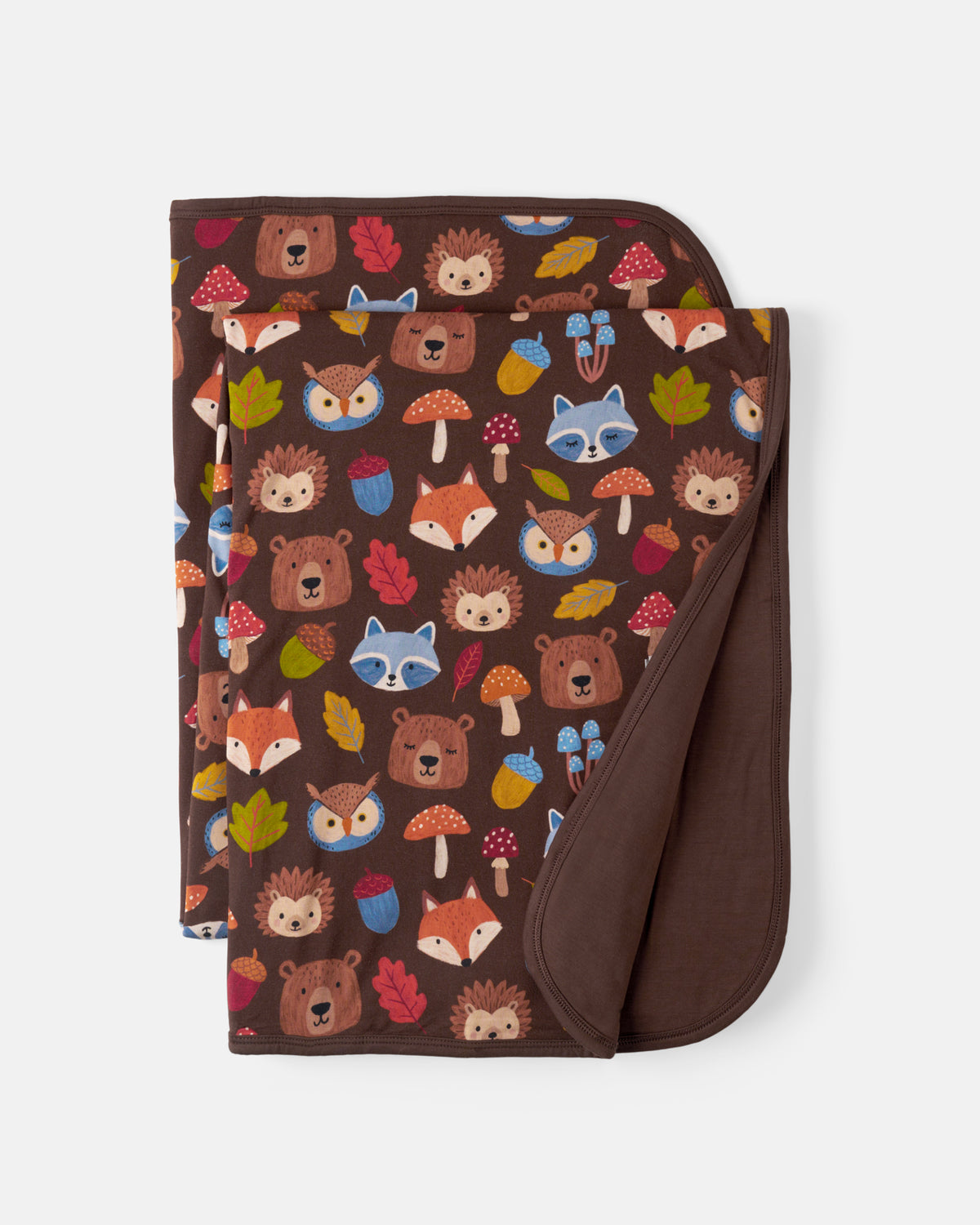 A folded blanket with a brown background and a colorful woodland animal print featuring bears, foxes, raccoons, hedgehogs, mushrooms, and leaves, with a solid brown reverse side, shown on a light gray background.