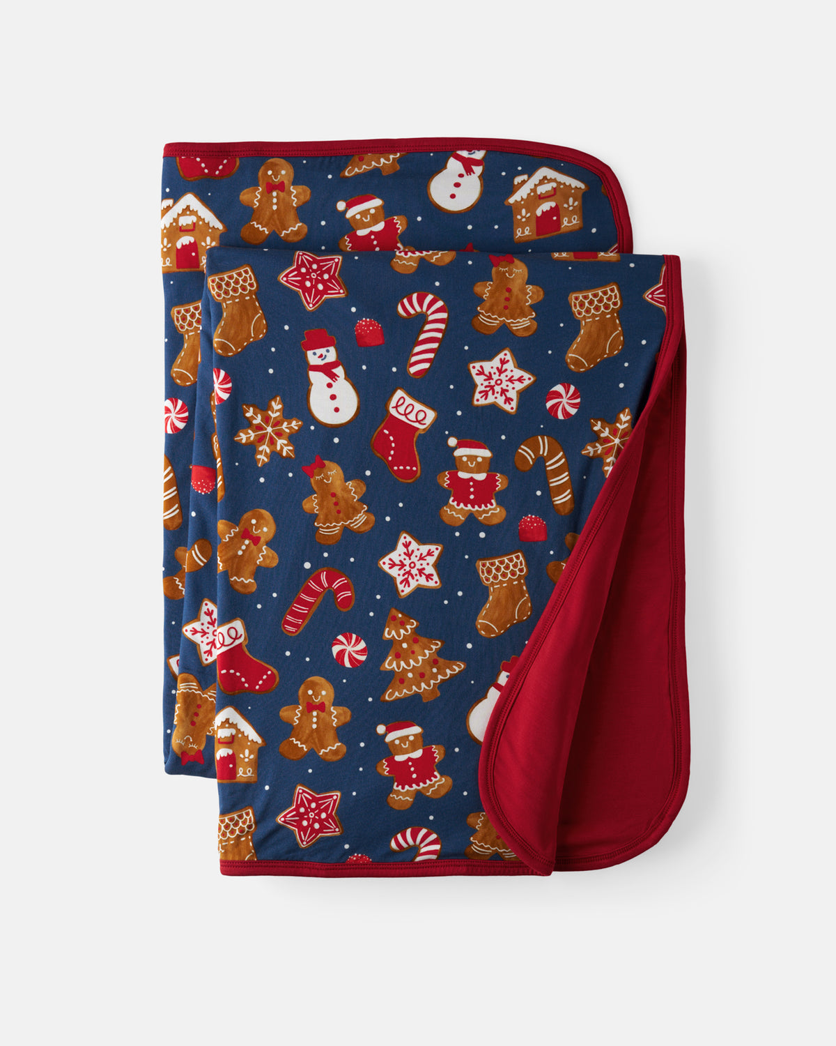 A folded Christmas-themed blanket with a navy blue background featuring gingerbread men, candy canes, snowmen, stockings, and stars, with a solid red reverse side, shown on a light gray background.