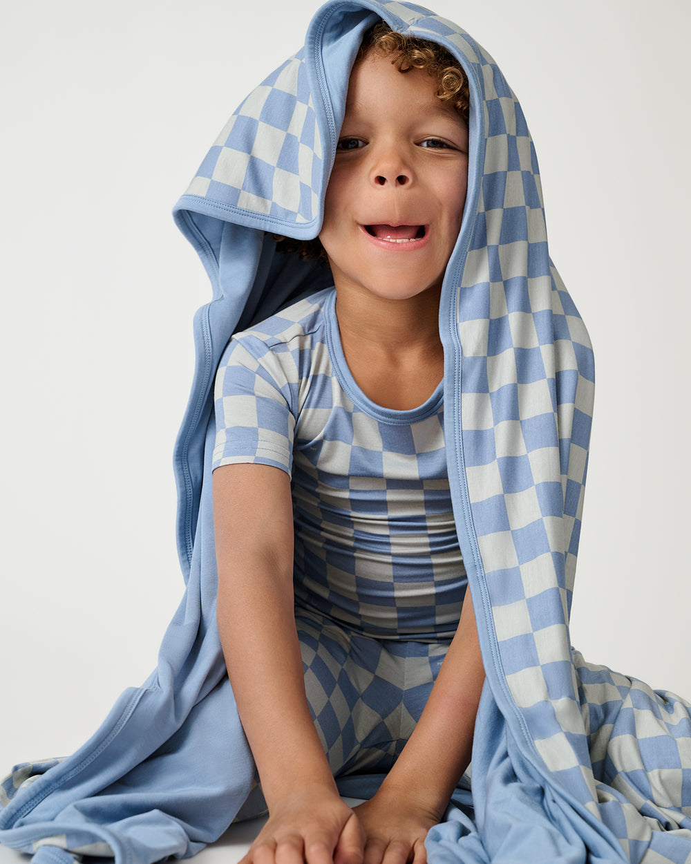Sitting boy with the Dusk Blue Checks Large Cloud Blanket® draped over him