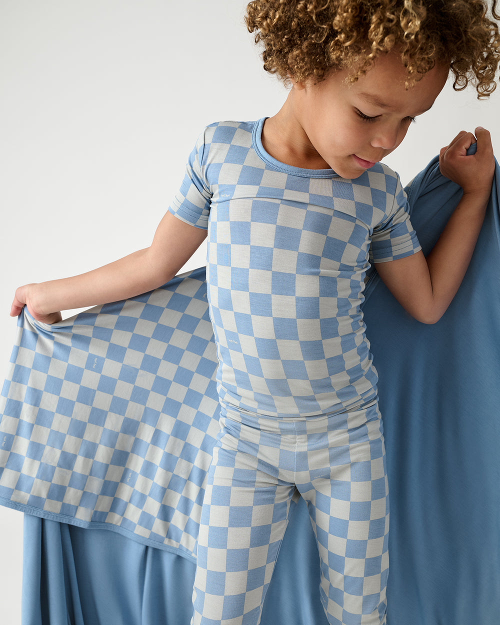 Boy holding the Dusk Blue Checks Large Cloud Blanket® wearing matching PJs