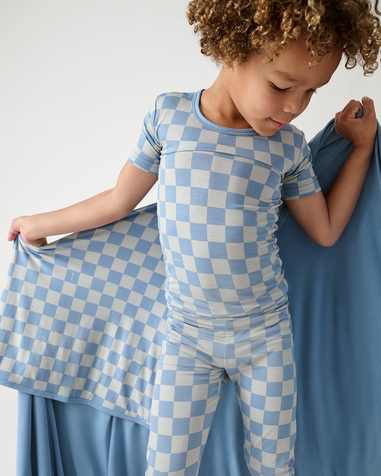 Boy holding the Dusk Blue Checks Large Cloud Blanket® wearing matching PJs