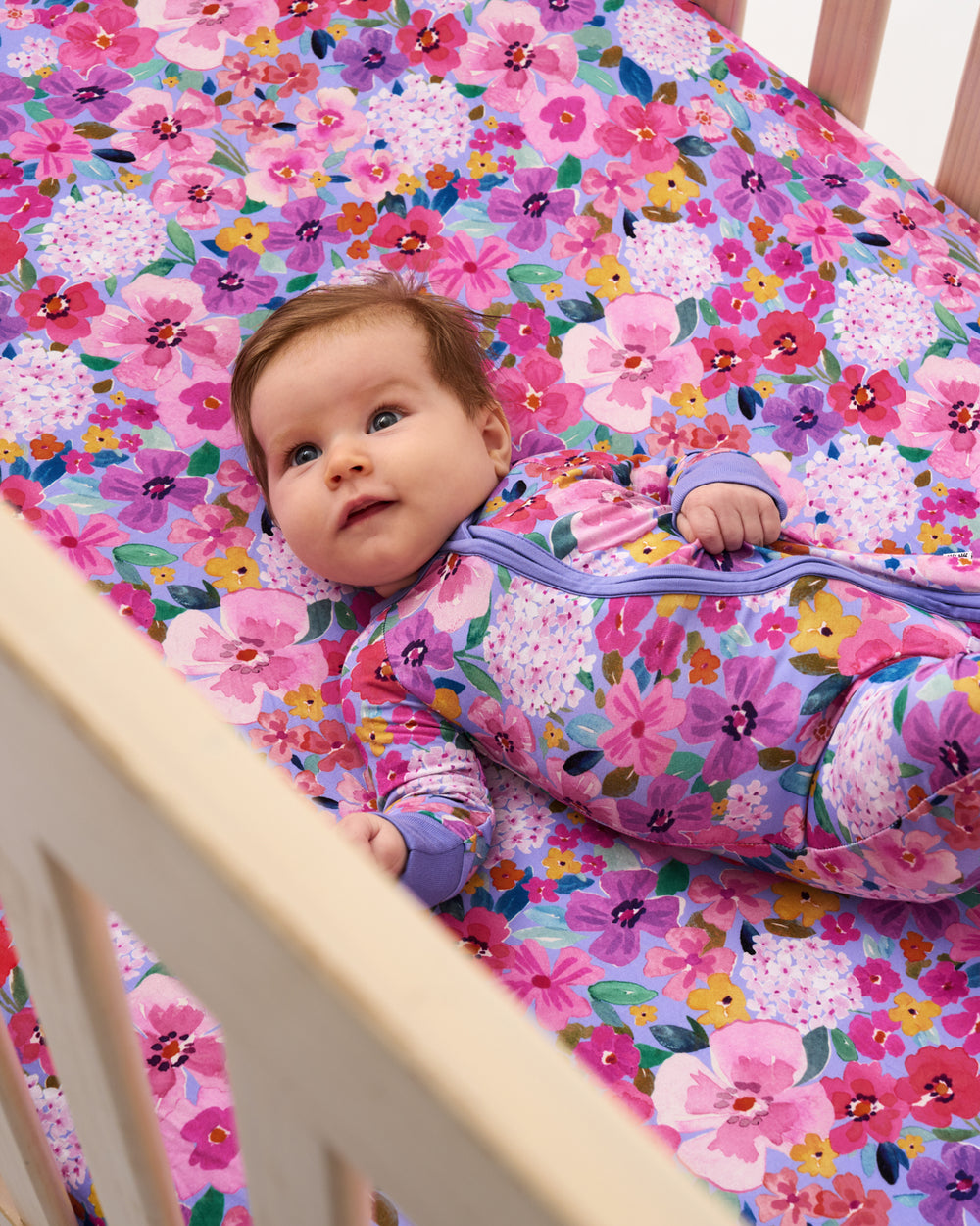 Baby laying on the Sweet Sprigs Fitted Crib Sheet wearing the matching floral zippy
