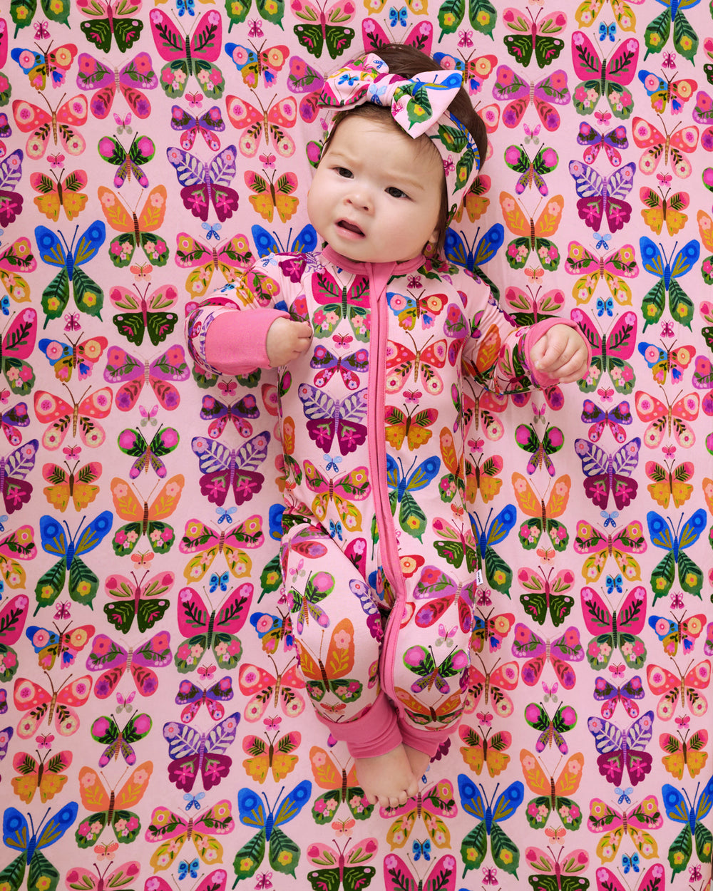 Baby laying on the Flutter Garden Fitted Crib Sheet wearing a matching zippy