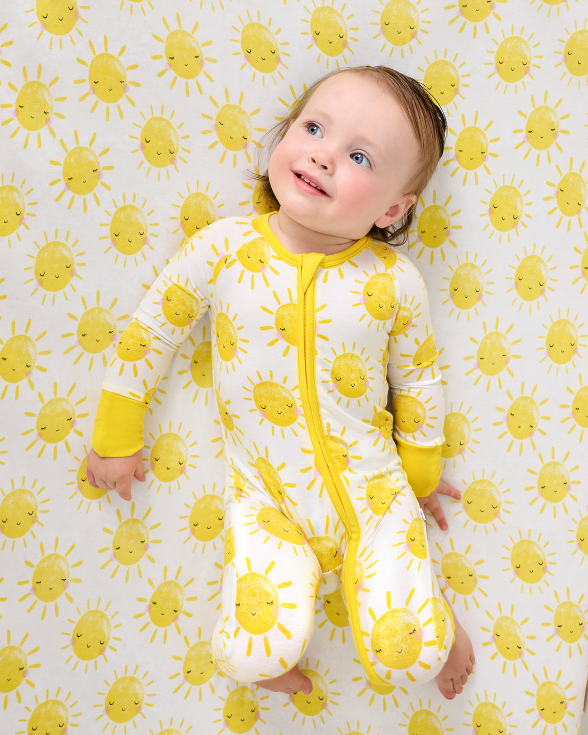 Baby wearing the Sunshine Zippy on a matching crib sheet