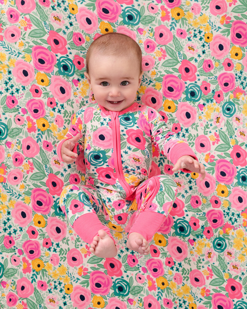 Baby laying on the Secret Garden Fitted Crib Sheet in a matching zippy