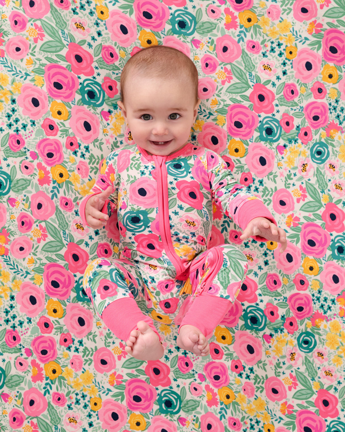 Baby laying on the Secret Garden Fitted Crib Sheet in a matching zippy