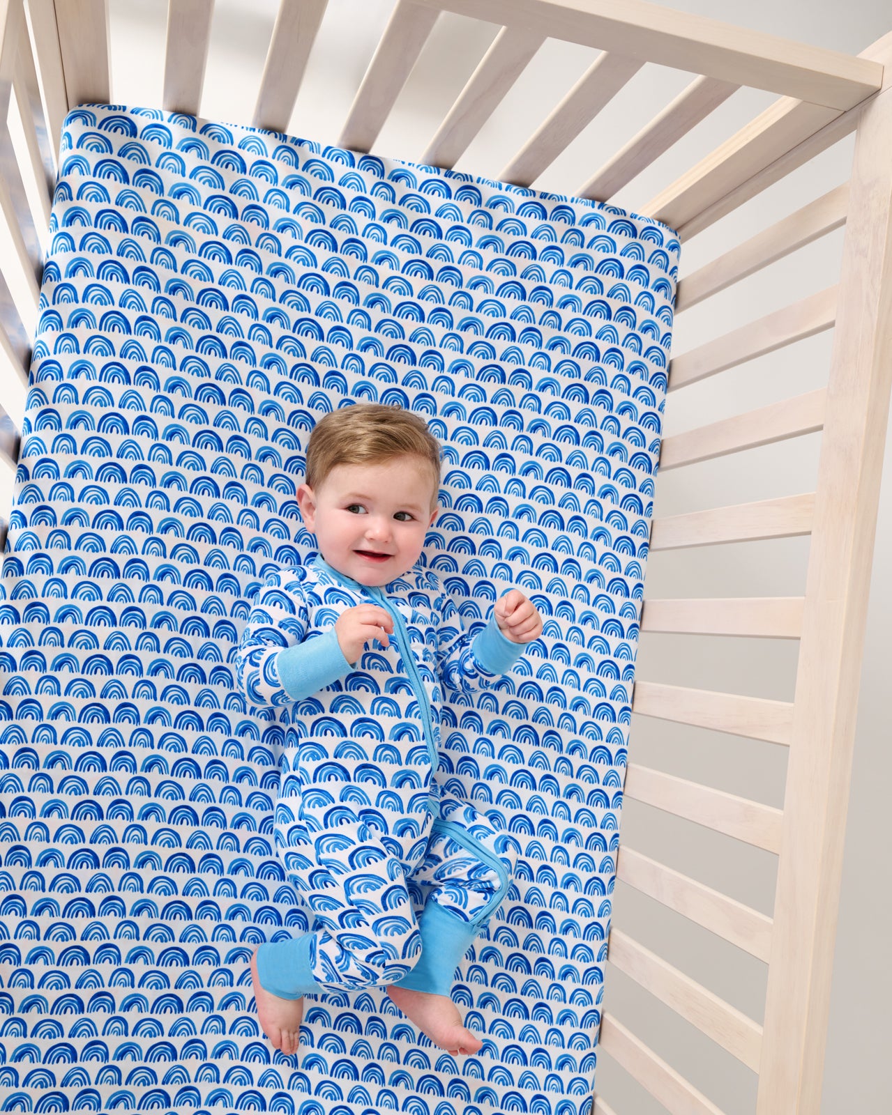 Aerial view of baby laying on the Blue Rainbows Fitted Crib Sheet