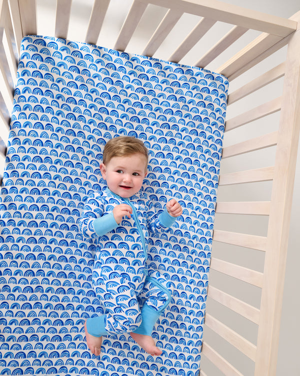 Aerial view of baby laying on the Blue Rainbows Fitted Crib Sheet